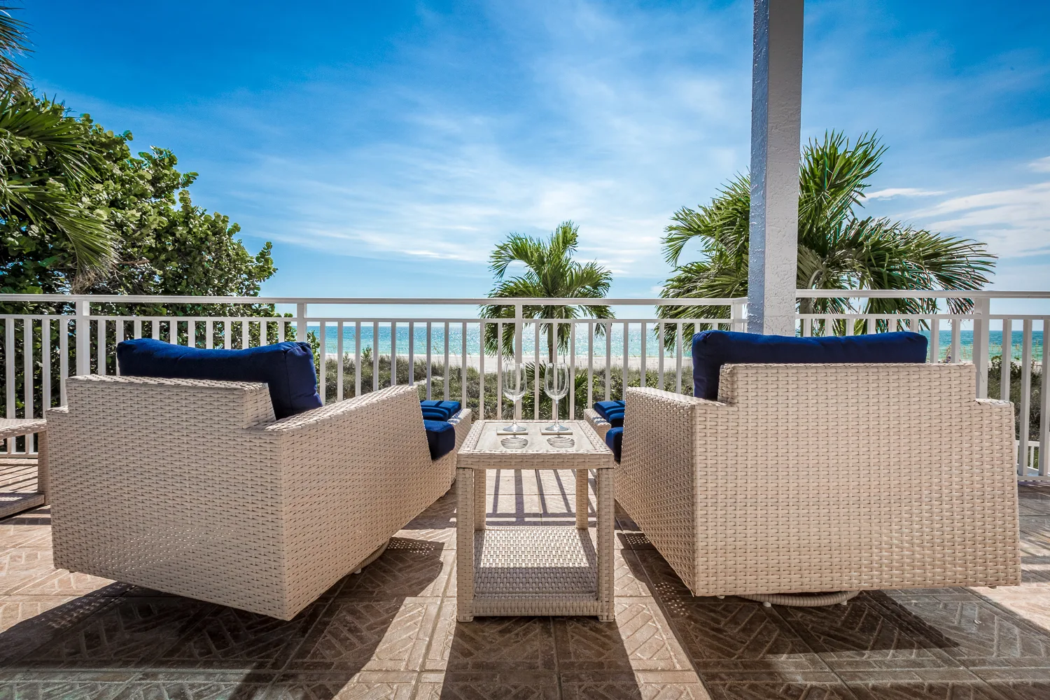 Covered balcony with white wicker seating overlooking palms and the beach