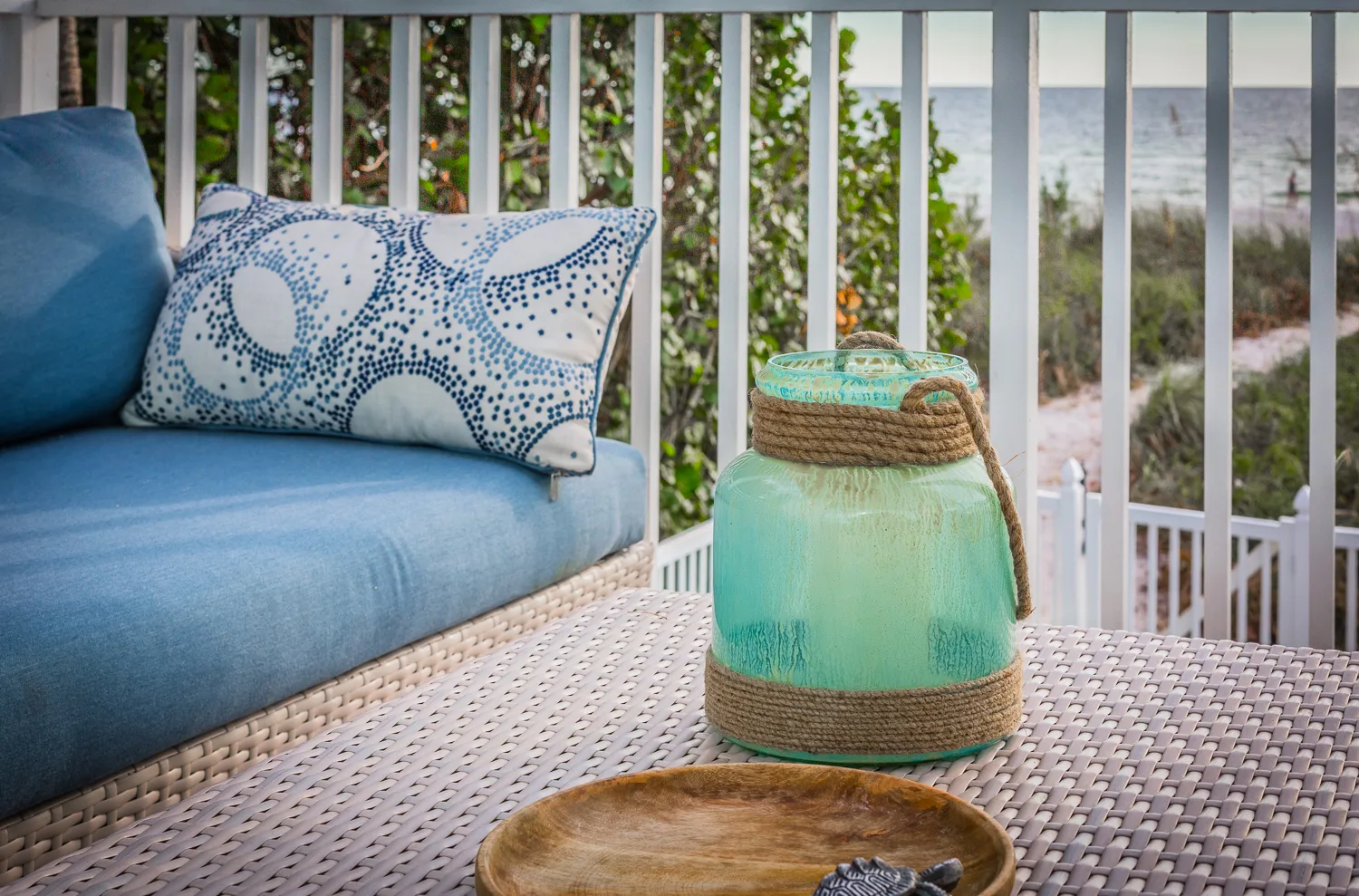 Blue daybed cushions and glass lantern on a railed deck near the water
