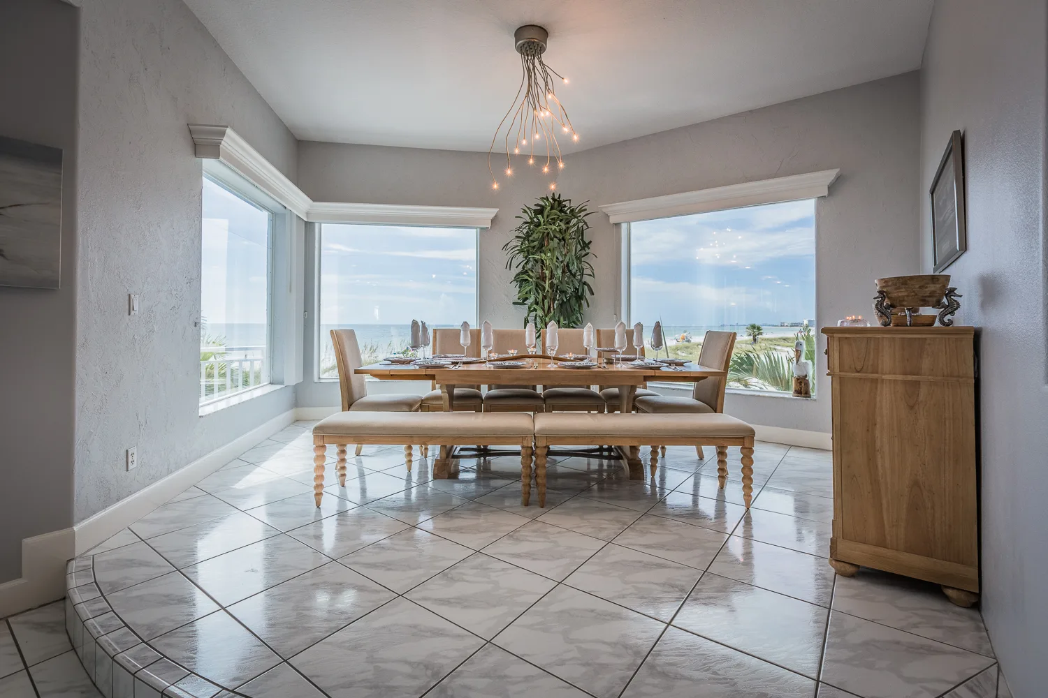 Dining room with long wooden table framed by panoramic water-view windows