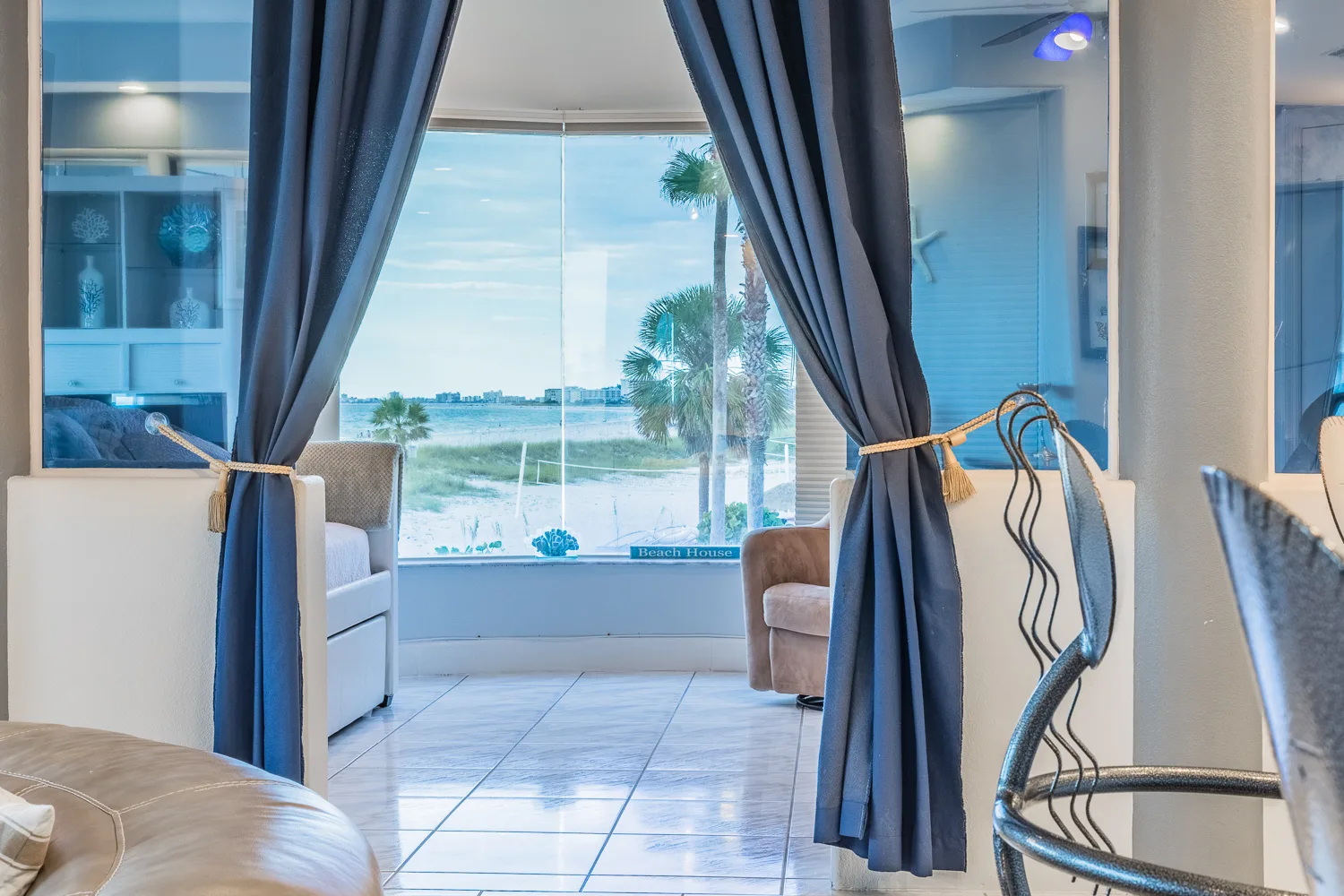 Blue curtains frame a bay window with beach views beyond the sitting area