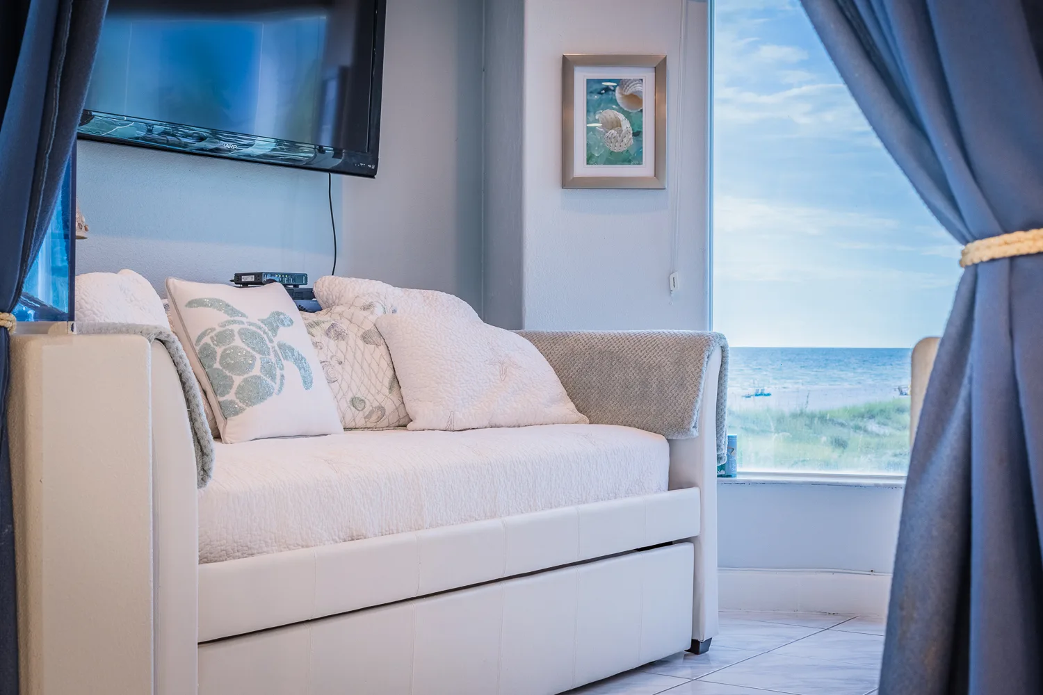 Daybed with sea turtle pillow and wall TV facing a beach-view window