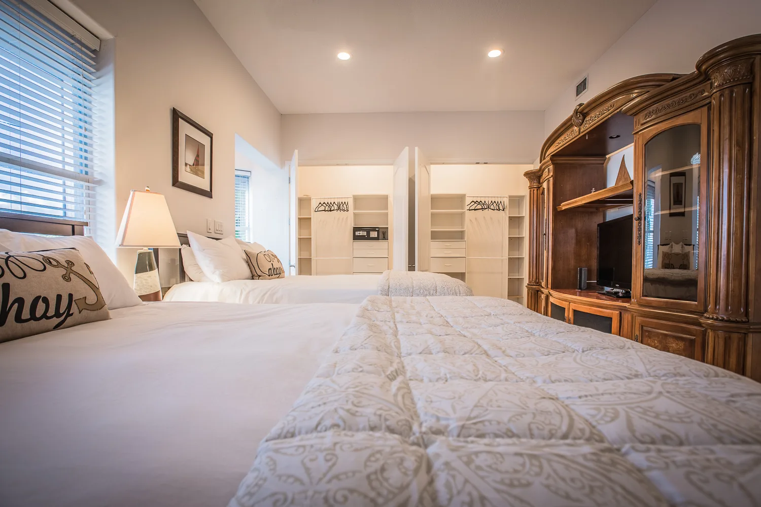 Bedroom with two beds, open shelving and a carved wood entertainment armoire