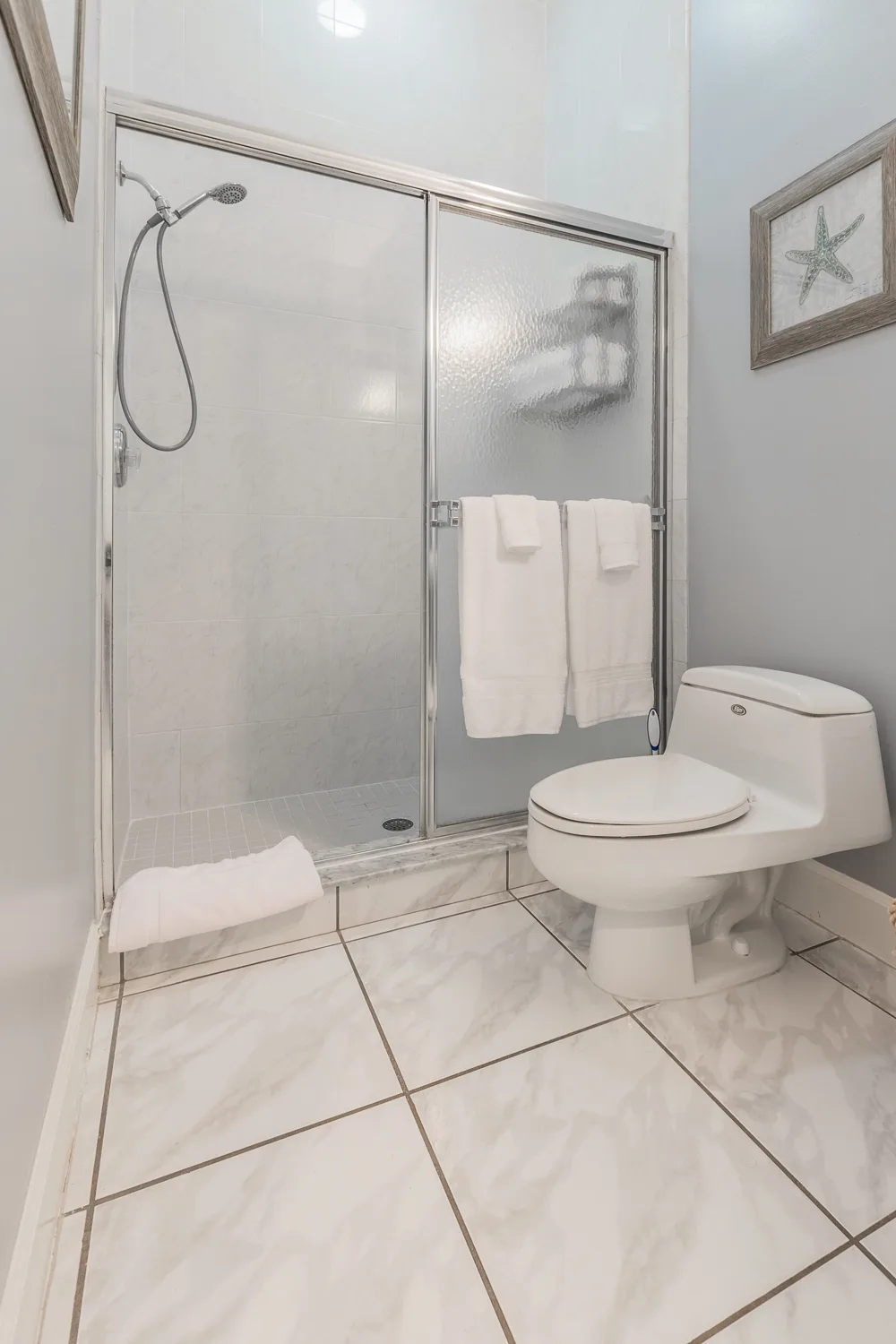 Bathroom with glass-door shower, white towels and starfish artwork