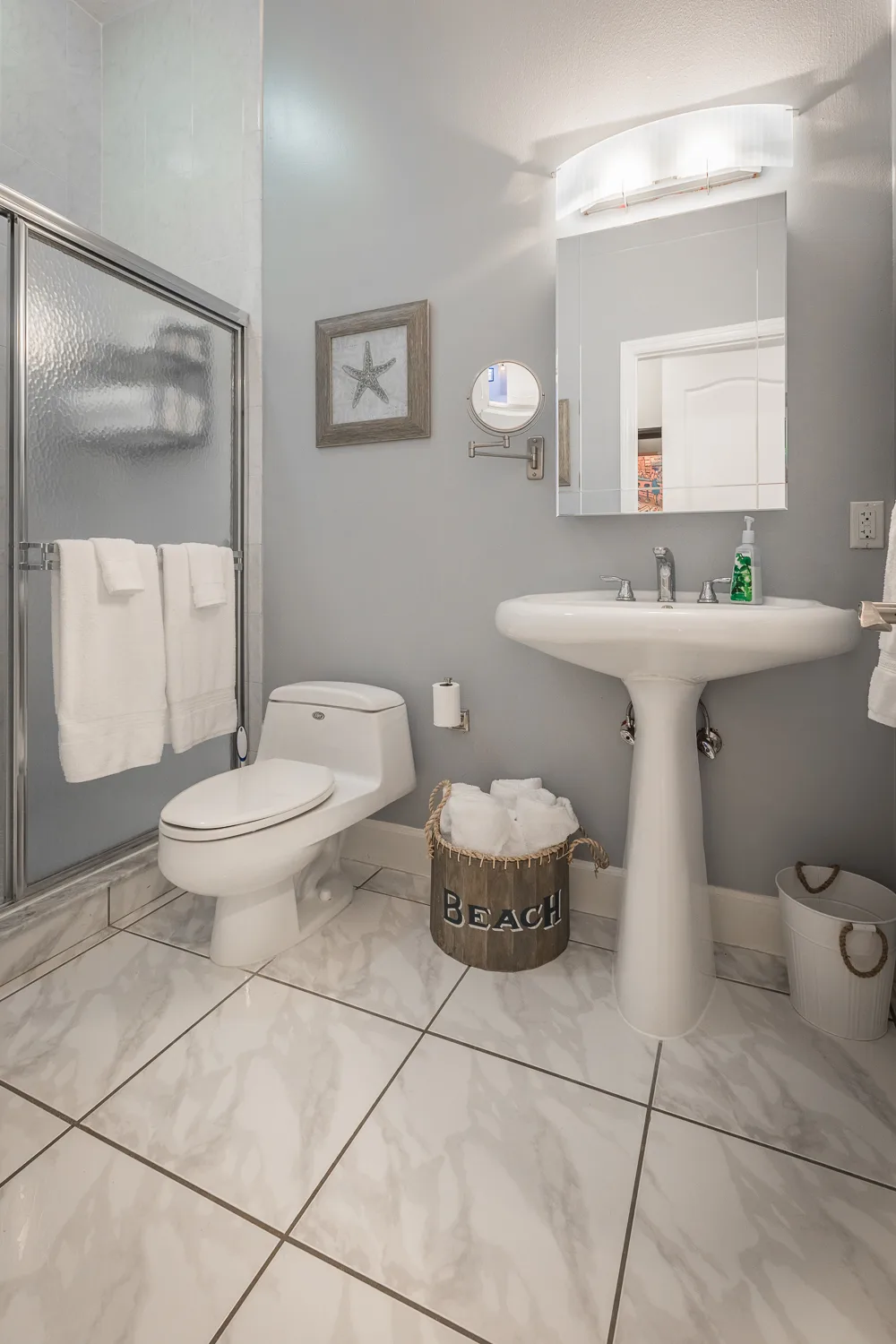 Bathroom with pedestal sink, glass shower and beach towel basket