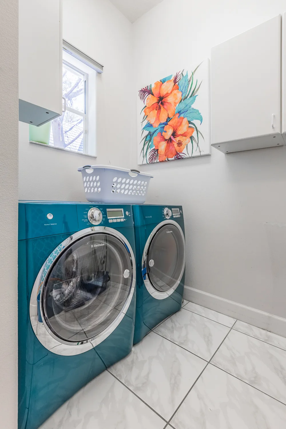 Laundry room with teal front-load washer and dryer beneath floral art