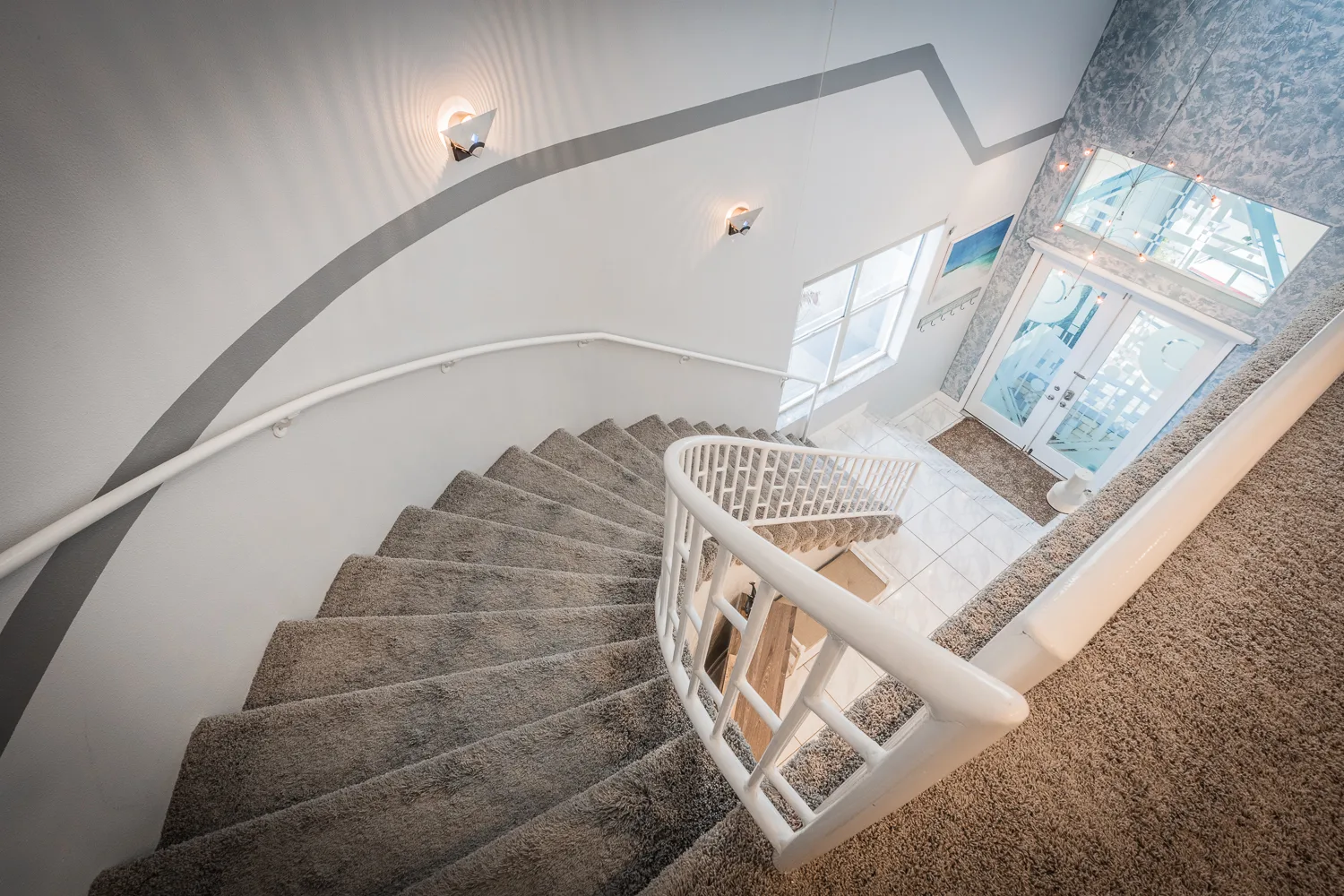 Curved carpeted staircase spiraling down to a bright tiled entry
