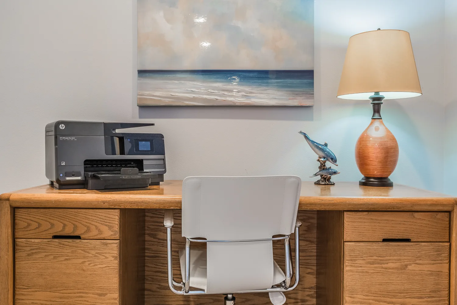 Oak desk with printer, dolphin figurine and seascape painting above