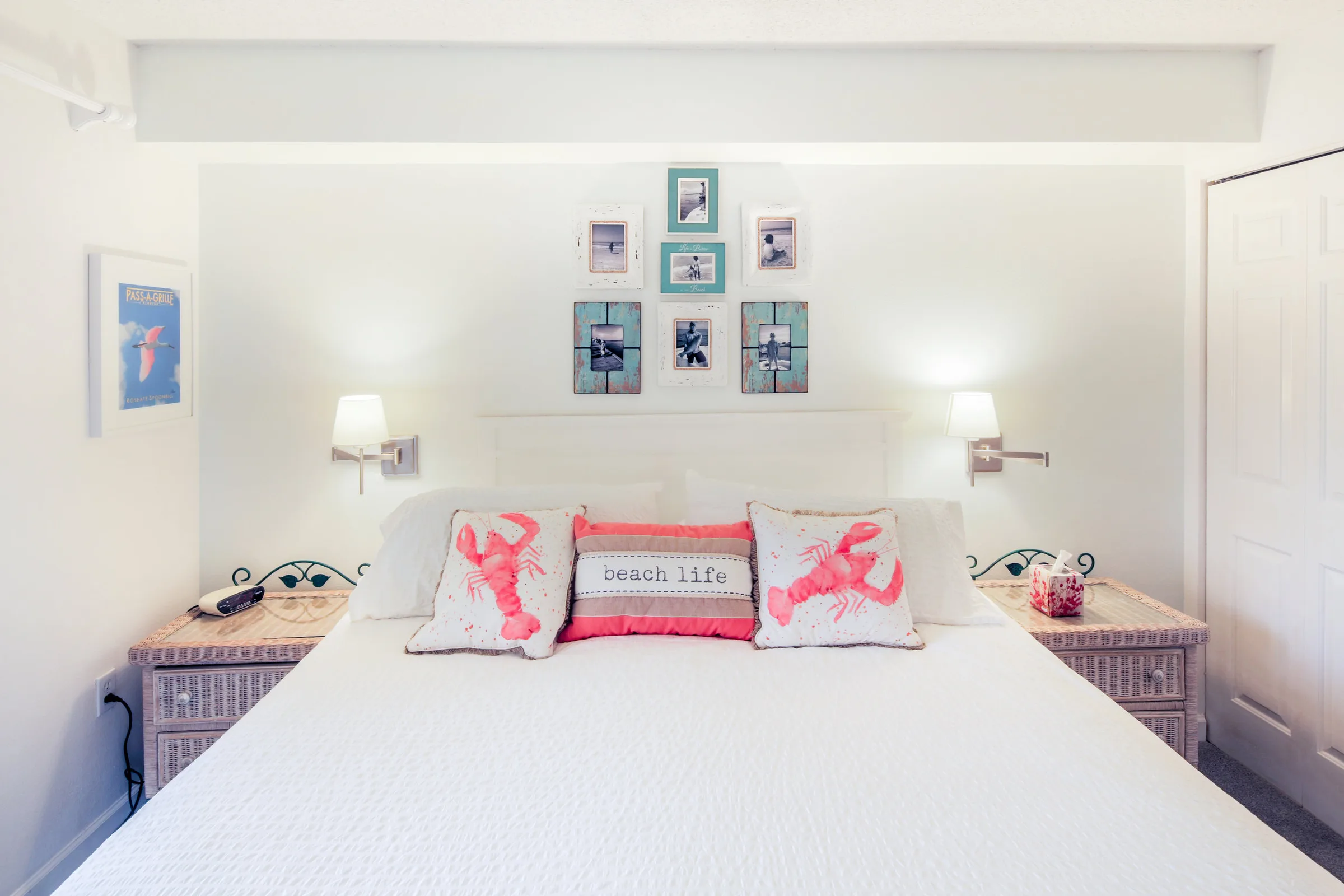 Crisp white bedroom with lobster accent pillows and framed beach photos