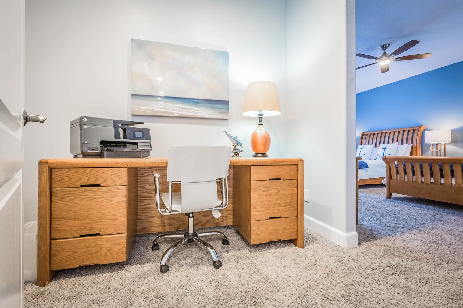 Office nook with oak desk and printer beside a blue bedroom