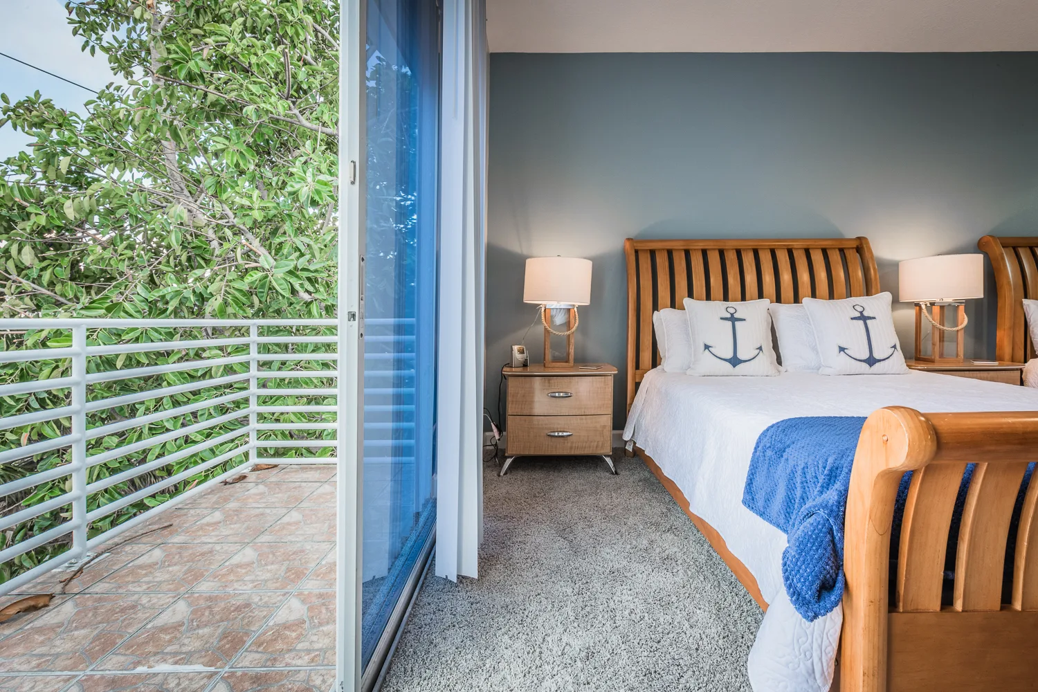 Bedroom with anchor pillows opening to a balcony among treetops