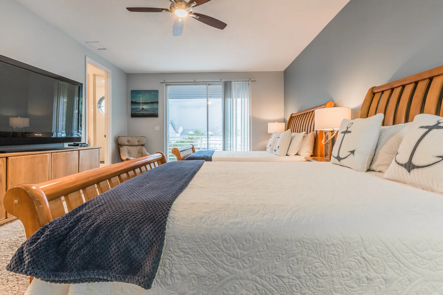 Two queen beds with navy throws facing a TV and balcony view