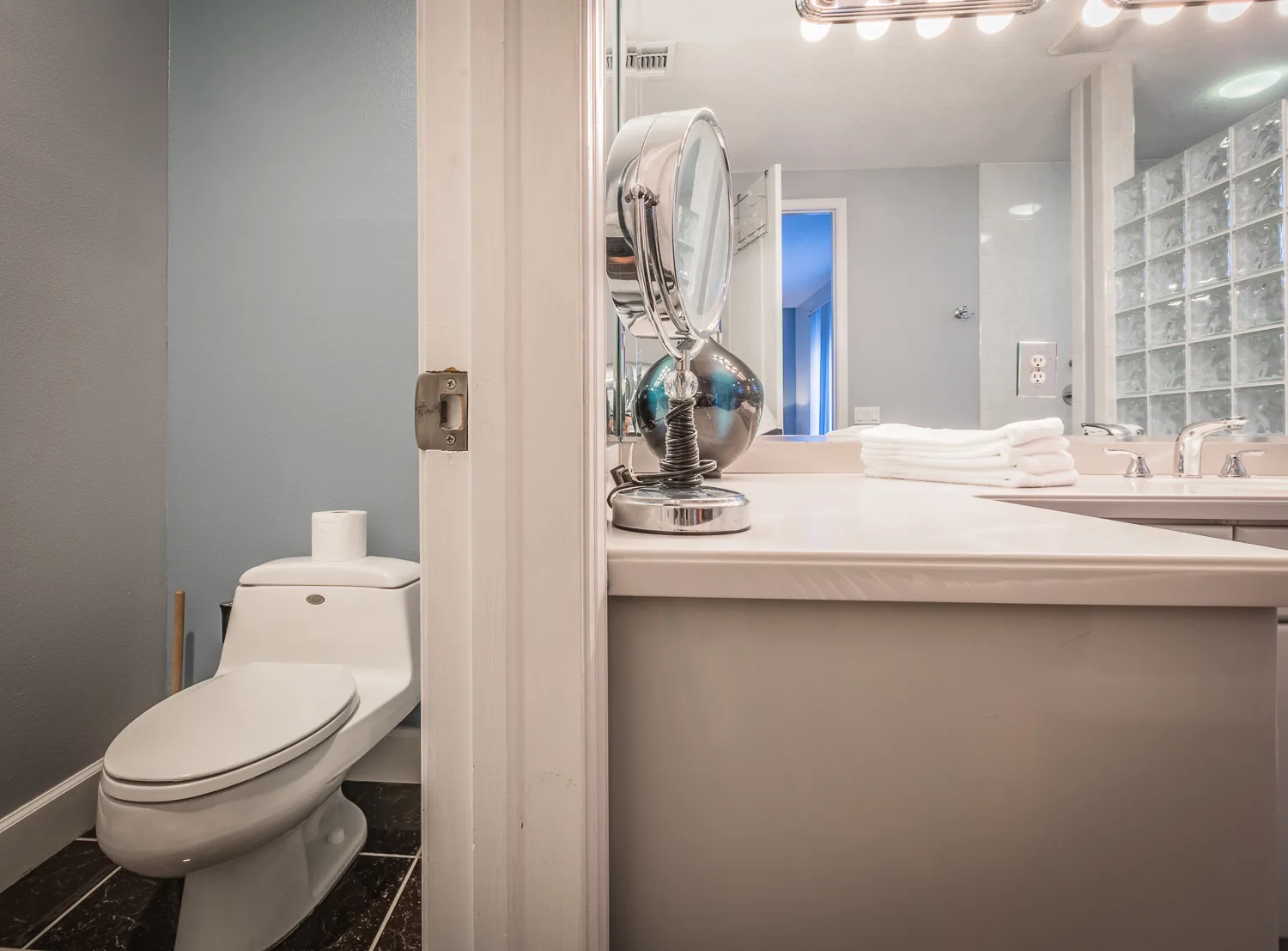 Bathroom vanity with mirror and toilet room seen through the doorway