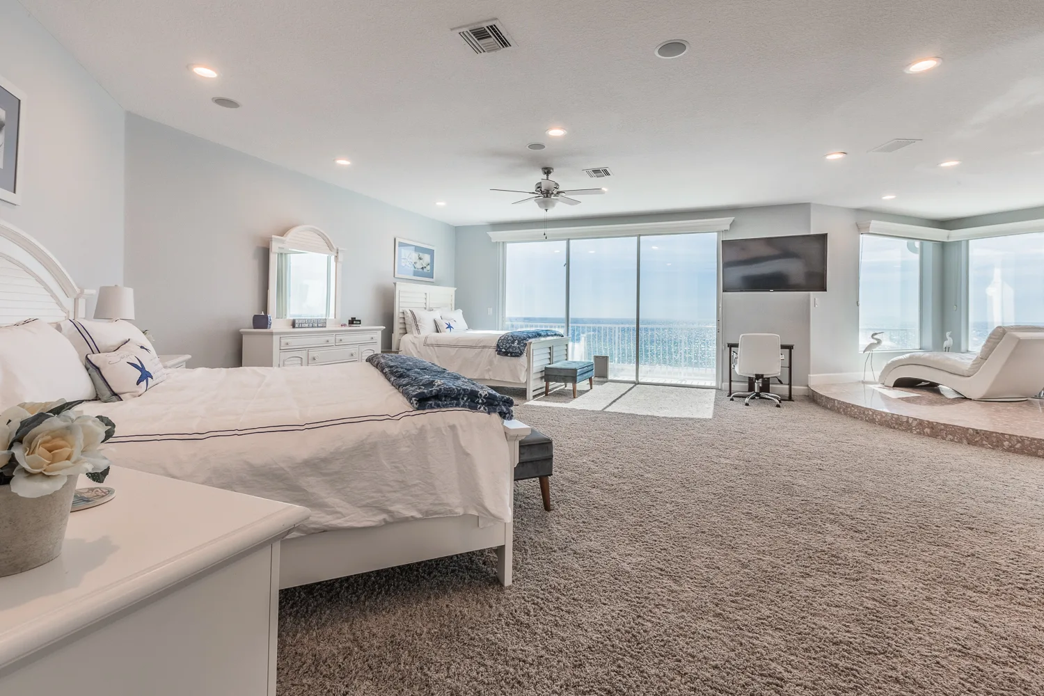 Large bedroom with two beds, chaise lounges and floor-to-ceiling water views