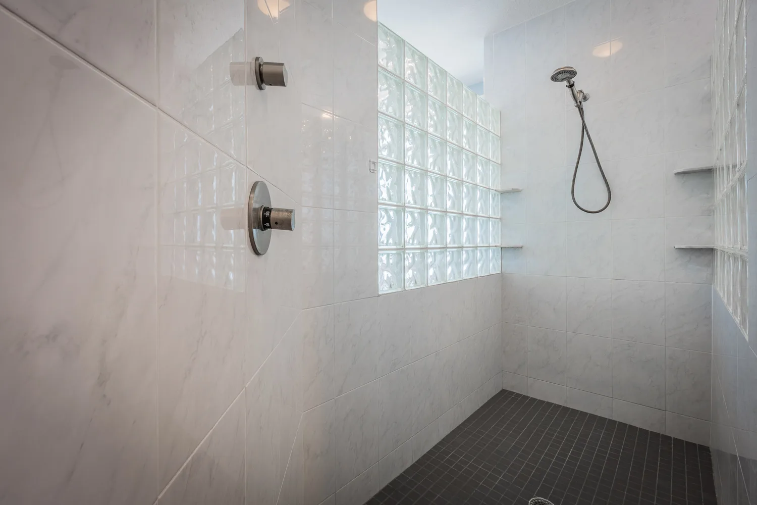 Walk-in shower with white tile, glass block wall and dark mosaic floor
