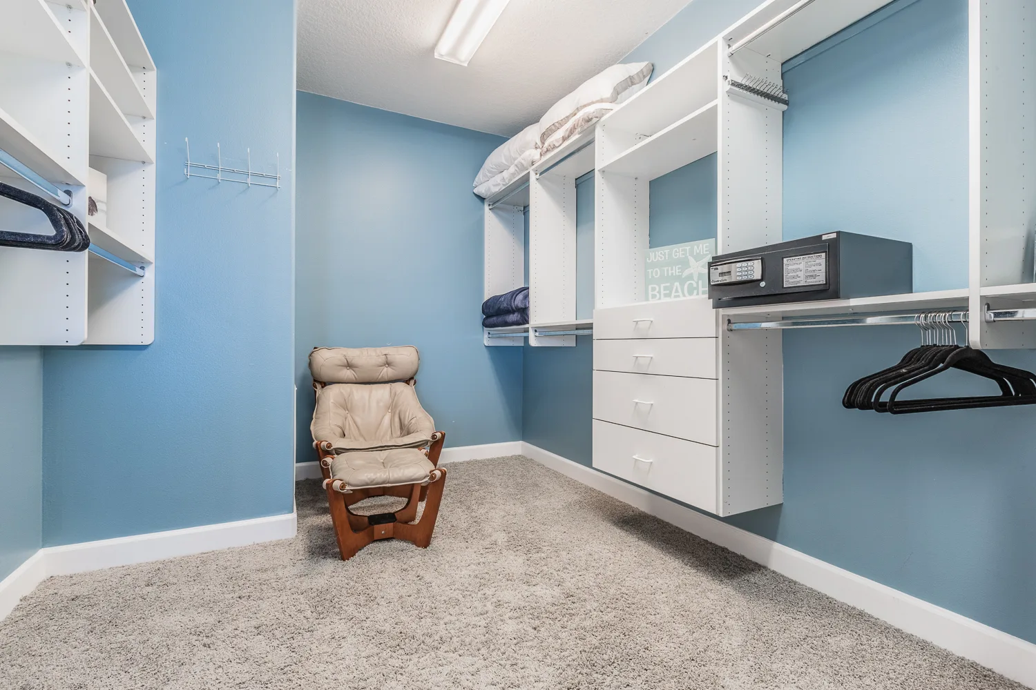 Blue walk-in closet with white shelving, safe and glider chair