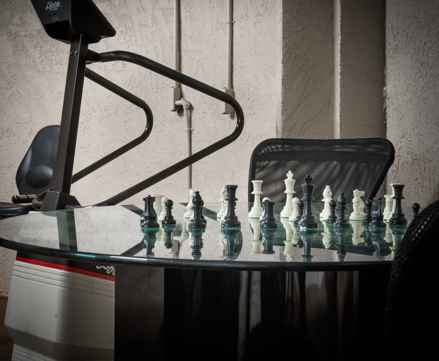 Chess set arranged on a glass table beside exercise equipment