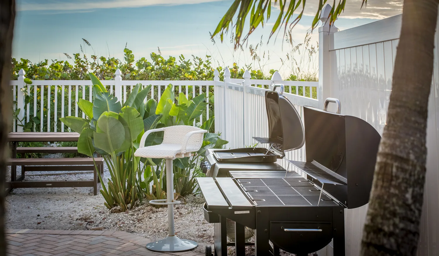 Two barbecue grills and bar stool on a fenced beachside patio