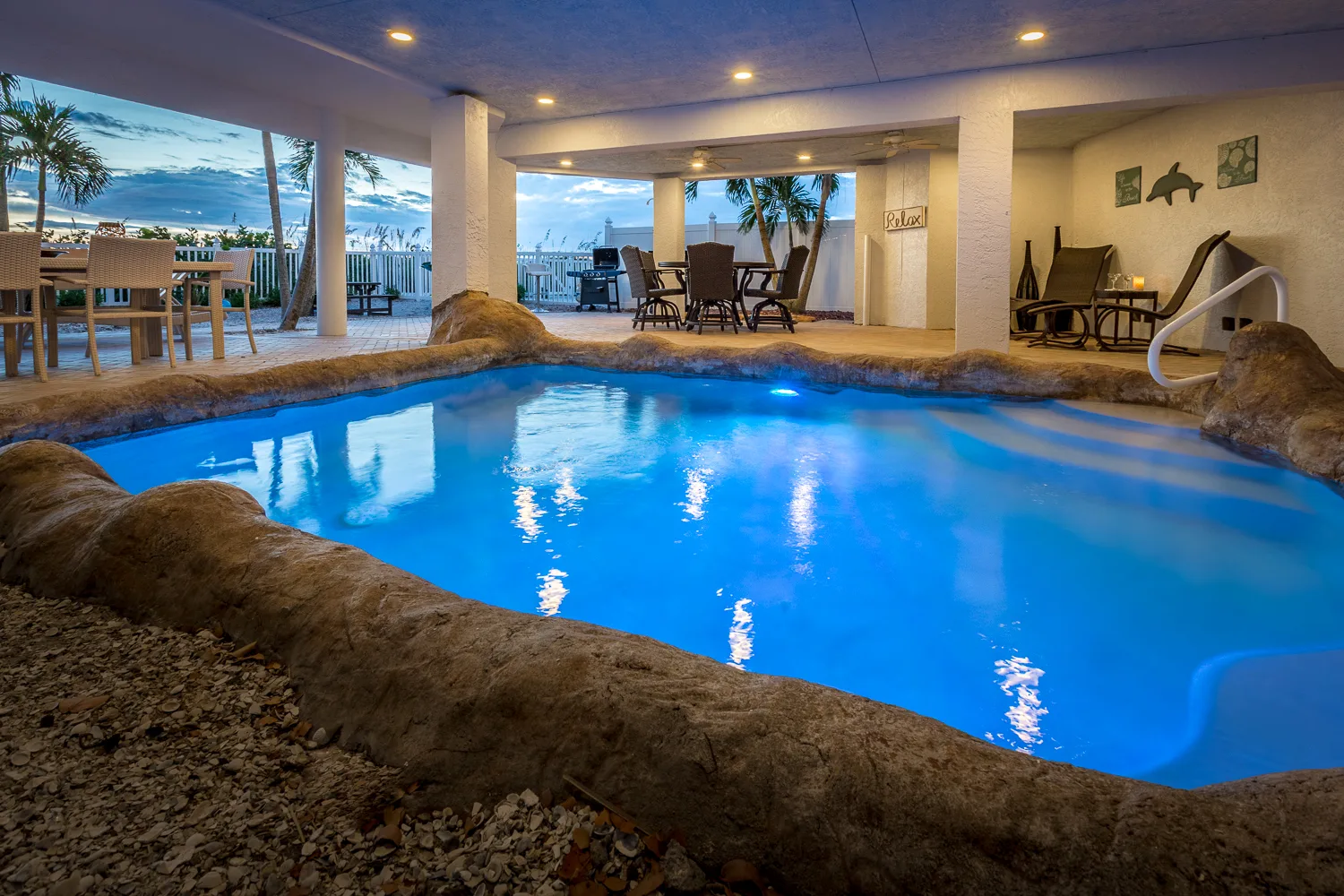 Lagoon-style pool glowing blue under a covered lanai at dusk