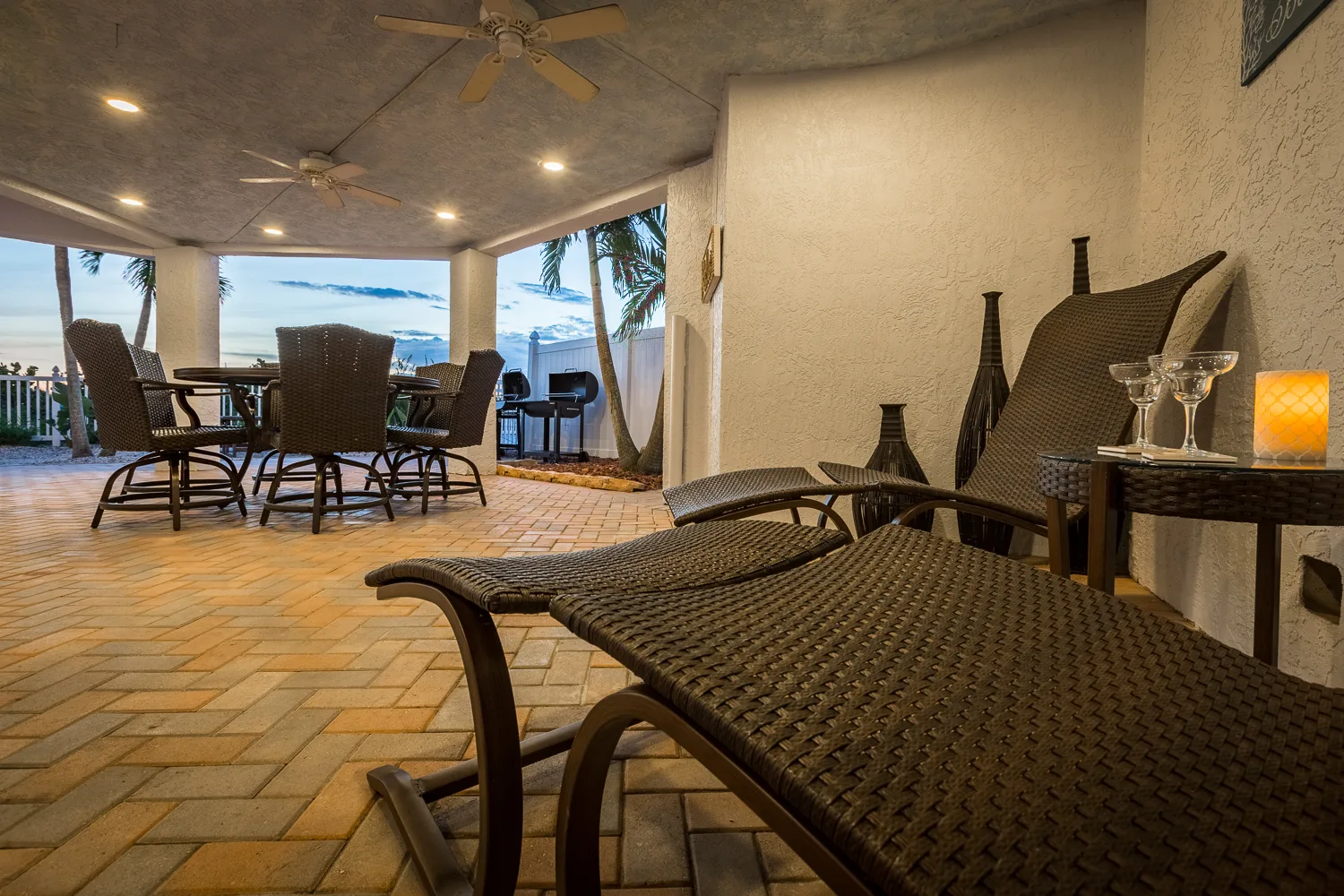Covered patio at dusk with wicker chaise lounges and dining table