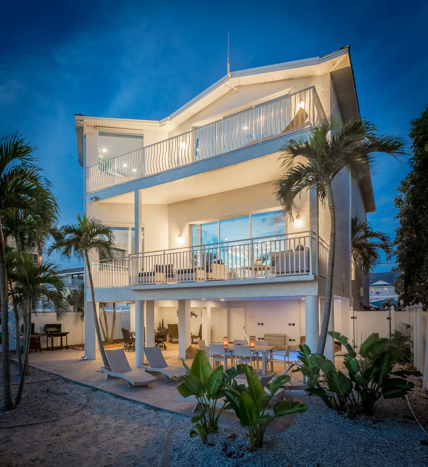 Three-story beach house lit at twilight with palms and double balconies