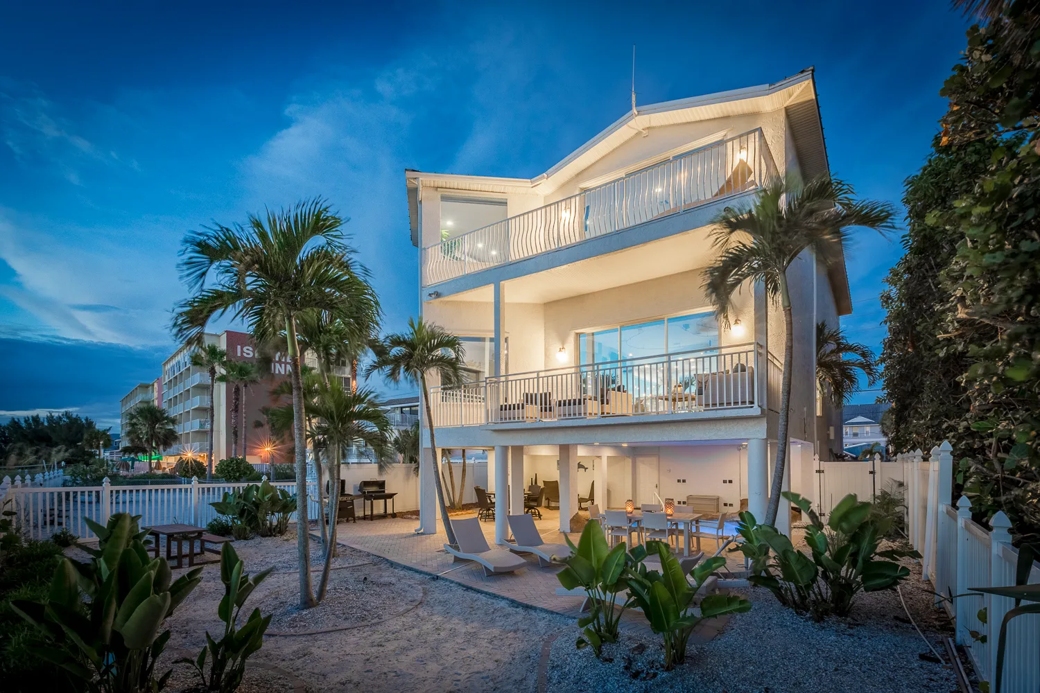 Beachfront home at dusk with balconies, palms and patio dining below