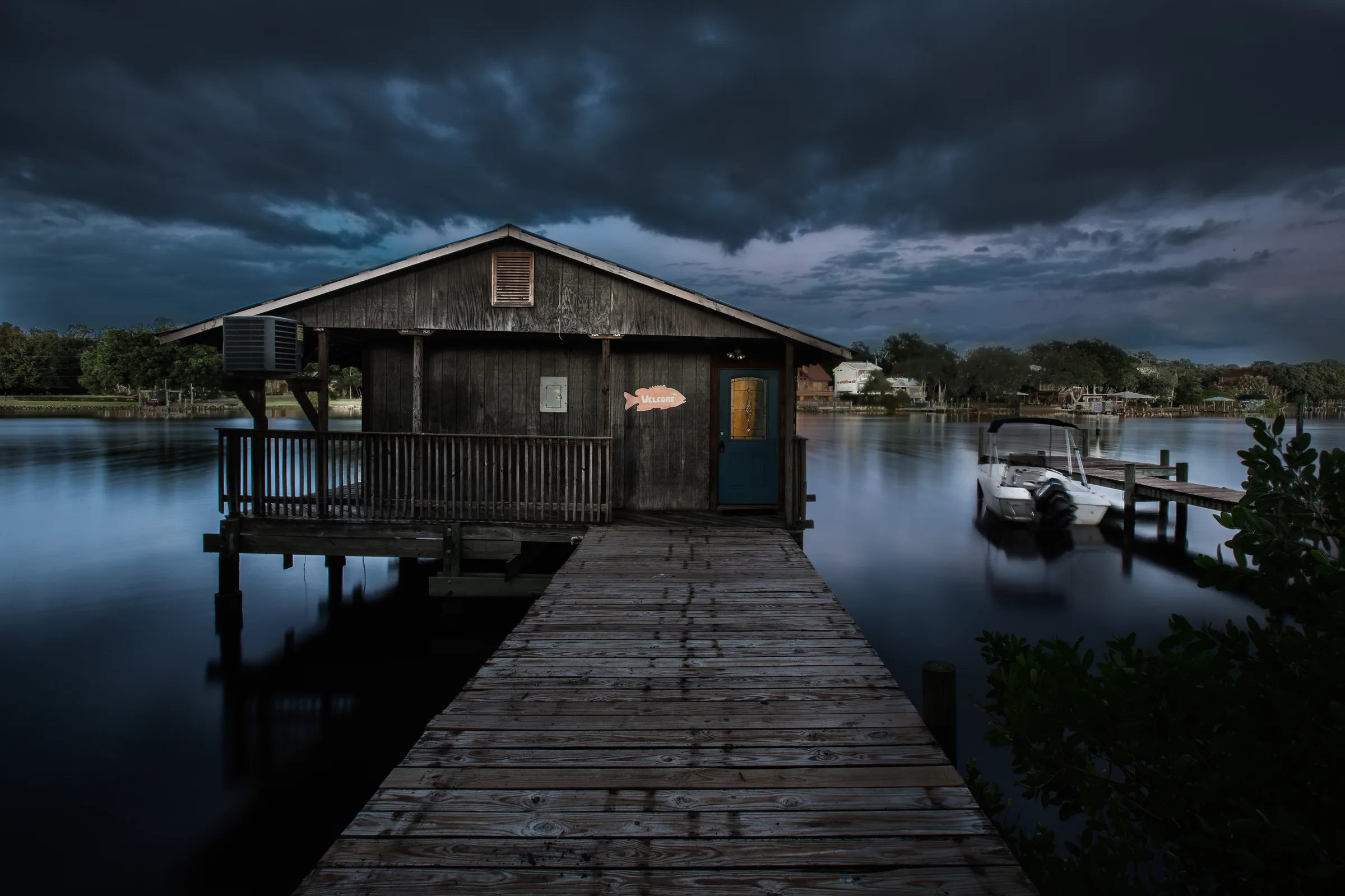 Storm clouds gathering over rustic boathouse, long dock and moored motorboat