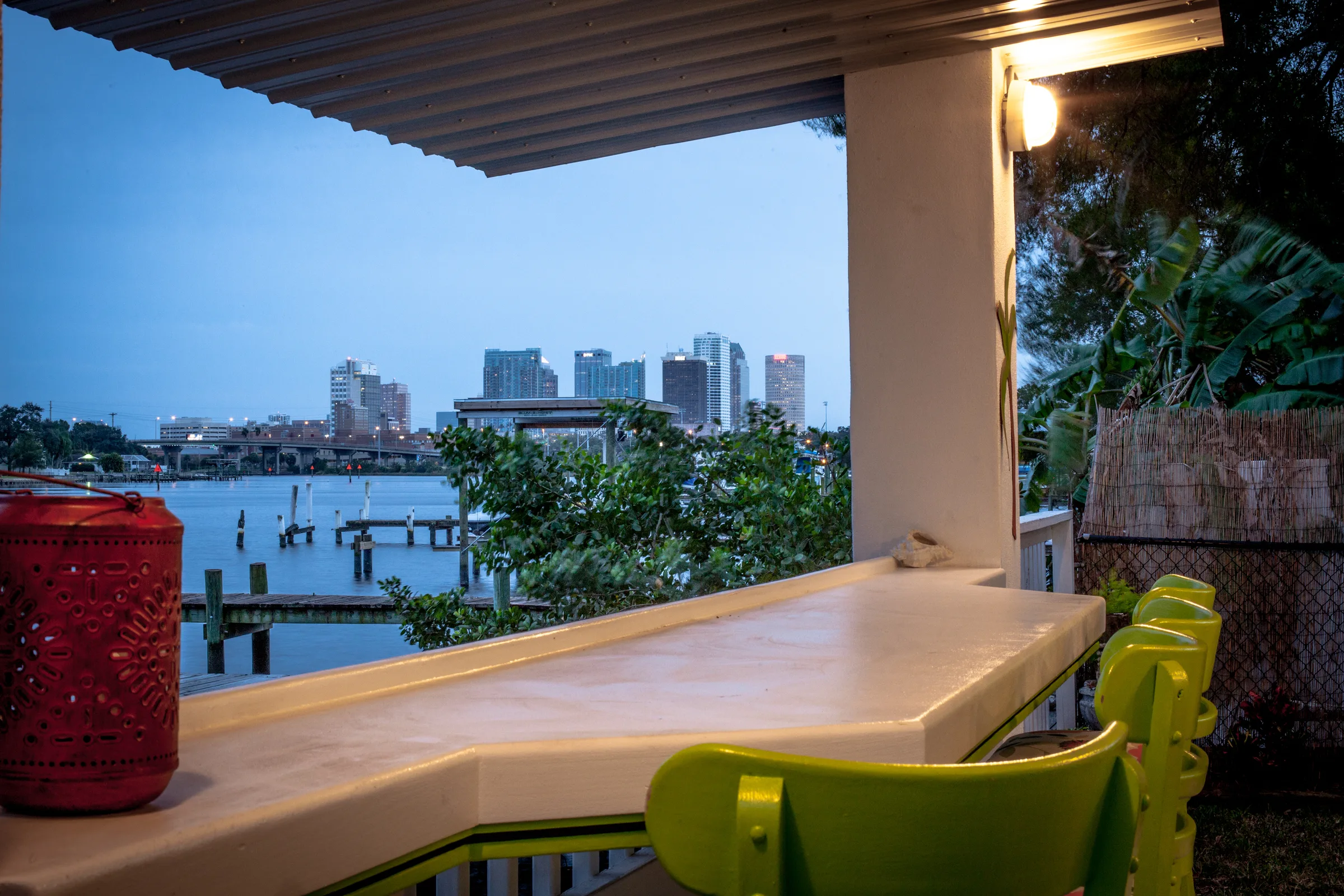 Waterside patio bar at dusk with green chairs and skyline across the bay