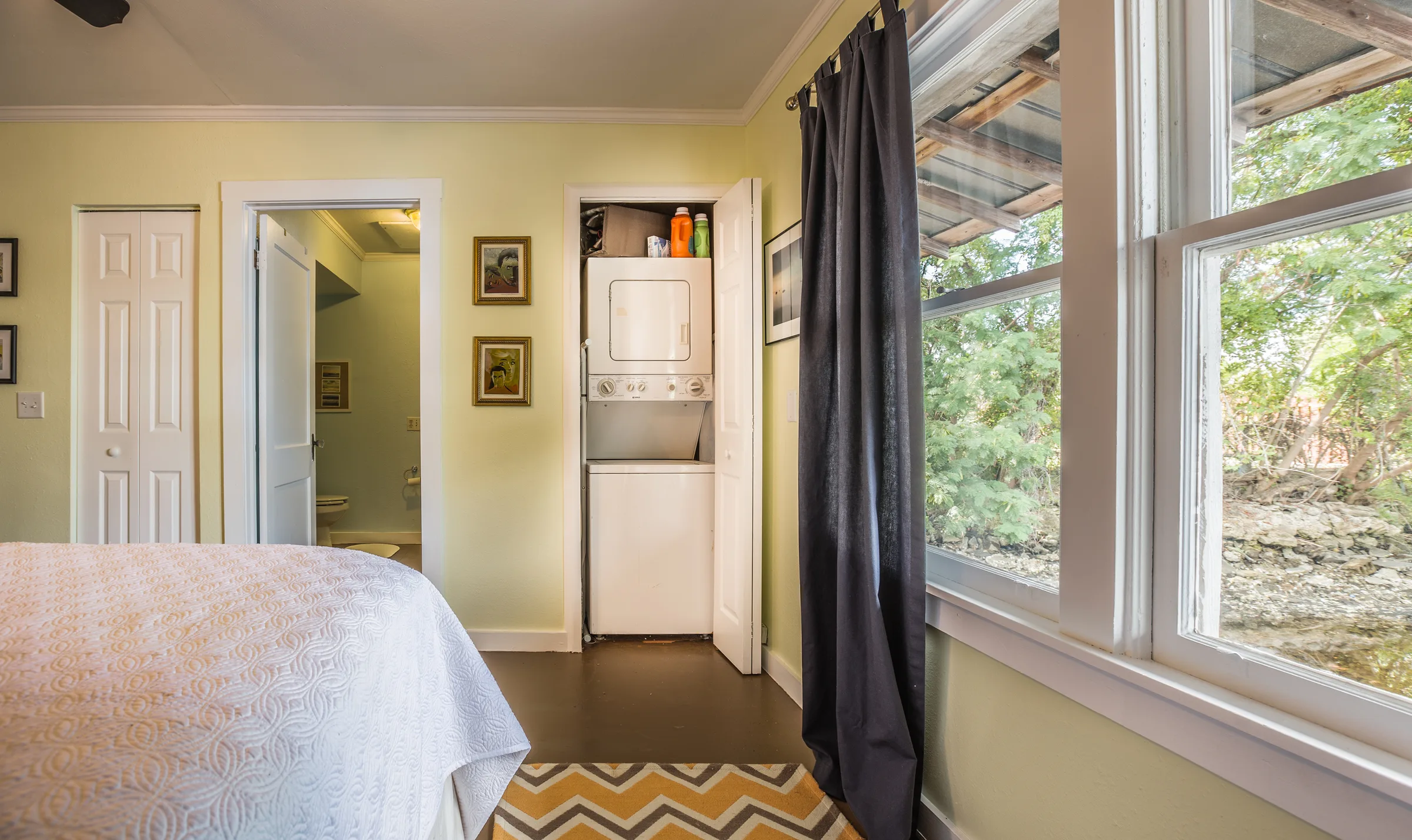 Sunny bedroom corner with stacked washer-dryer closet and wooded window view