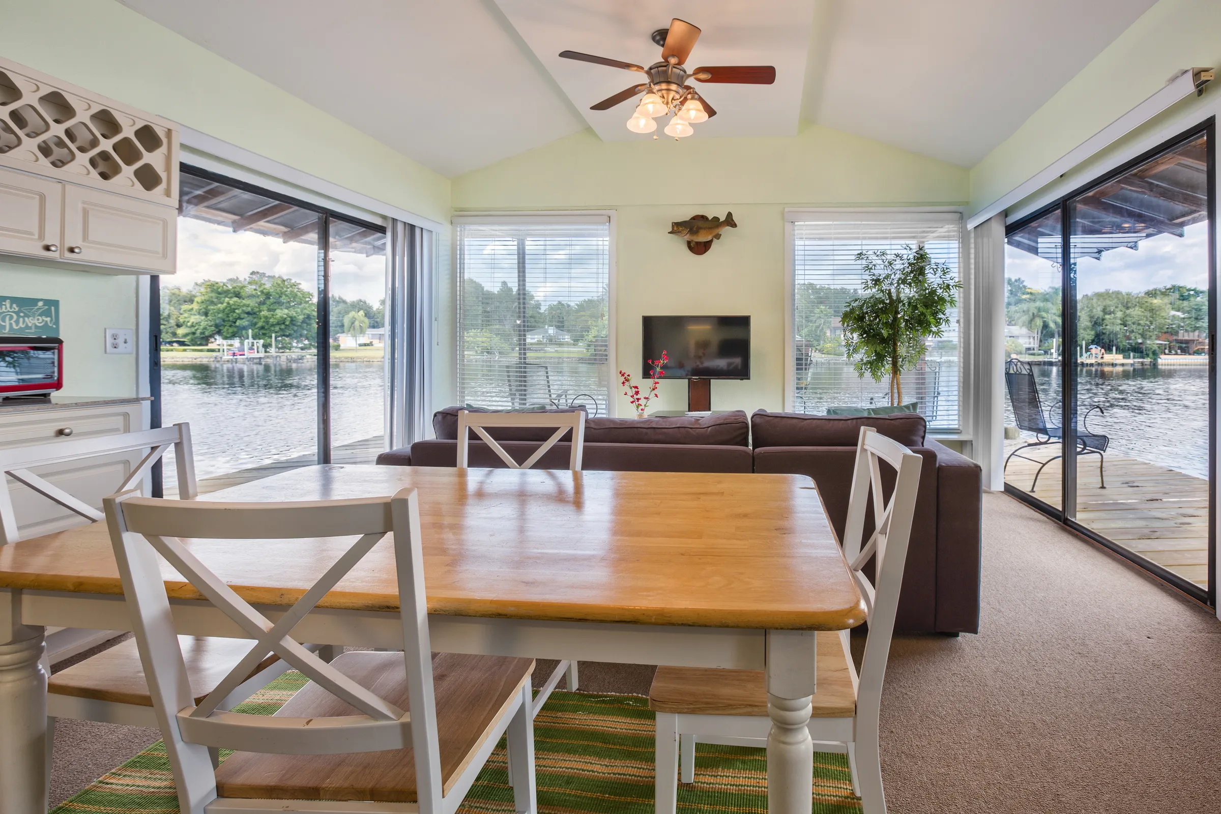 Vaulted dining and living room wrapped in glass doors with lake views