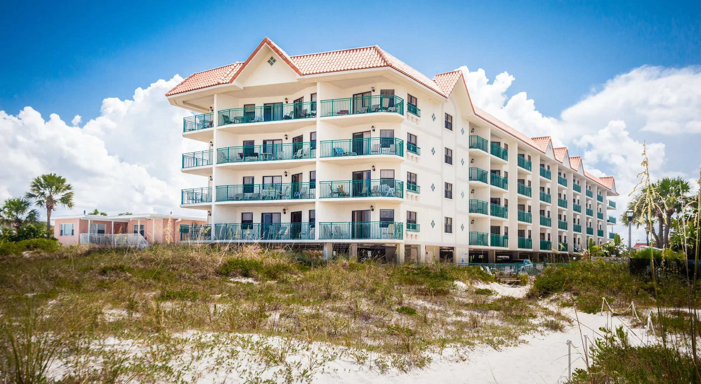 Tile-roofed beachfront condo building rising behind grassy sand dunes