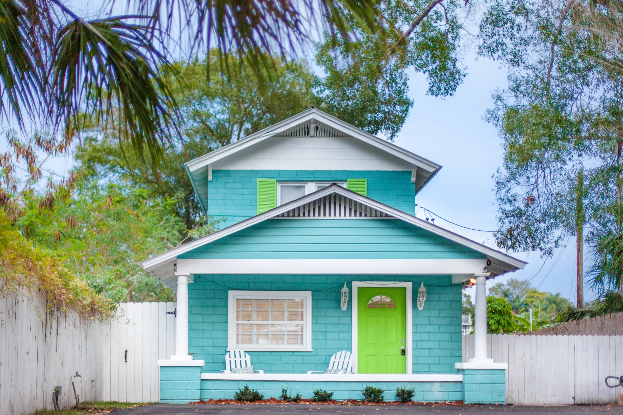 Turquoise cottage with lime green front door and white porch chairs