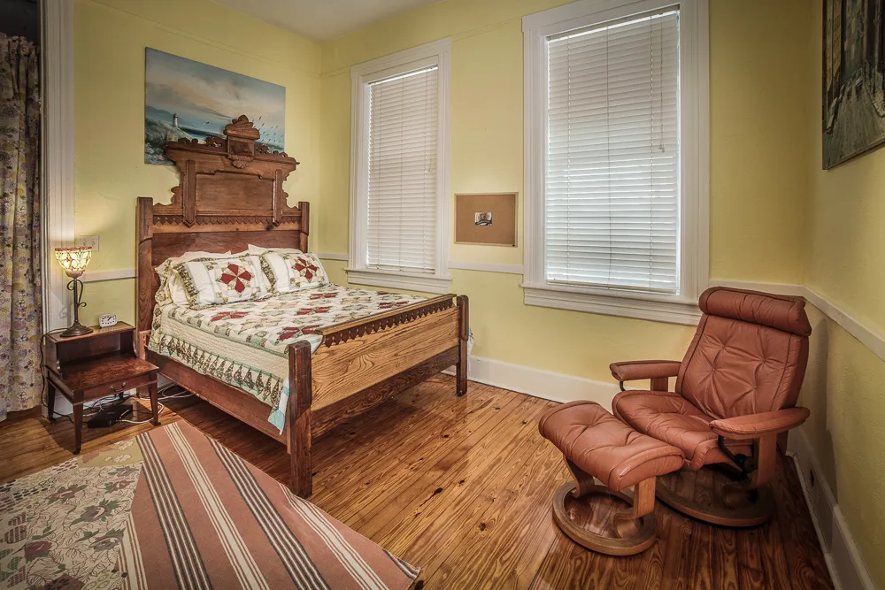 Antique carved wood bed and leather recliner in sunny yellow bedroom