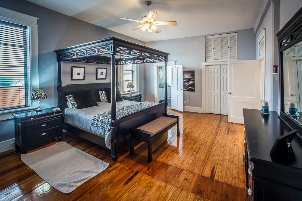 Gray bedroom with black four-poster bed and gleaming heart-pine floors