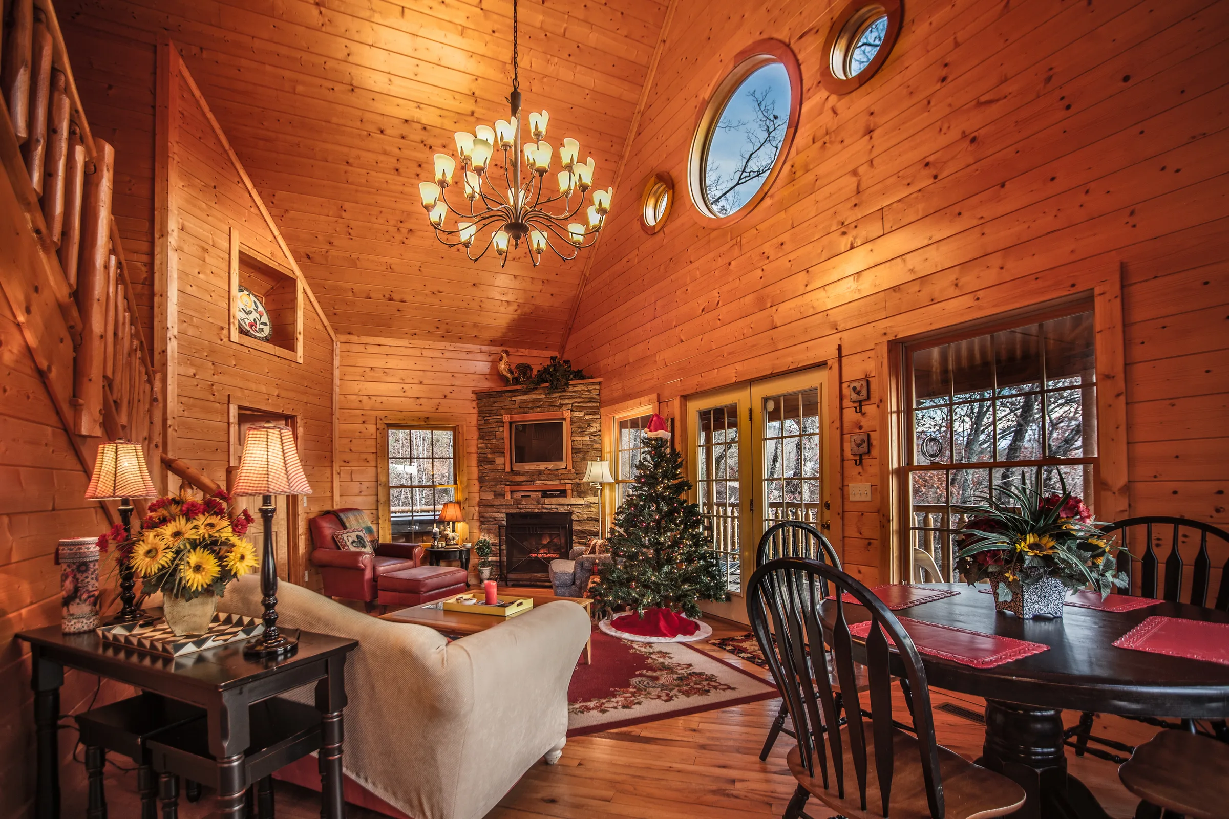 Log cabin great room with chandelier, stone fireplace and Christmas tree