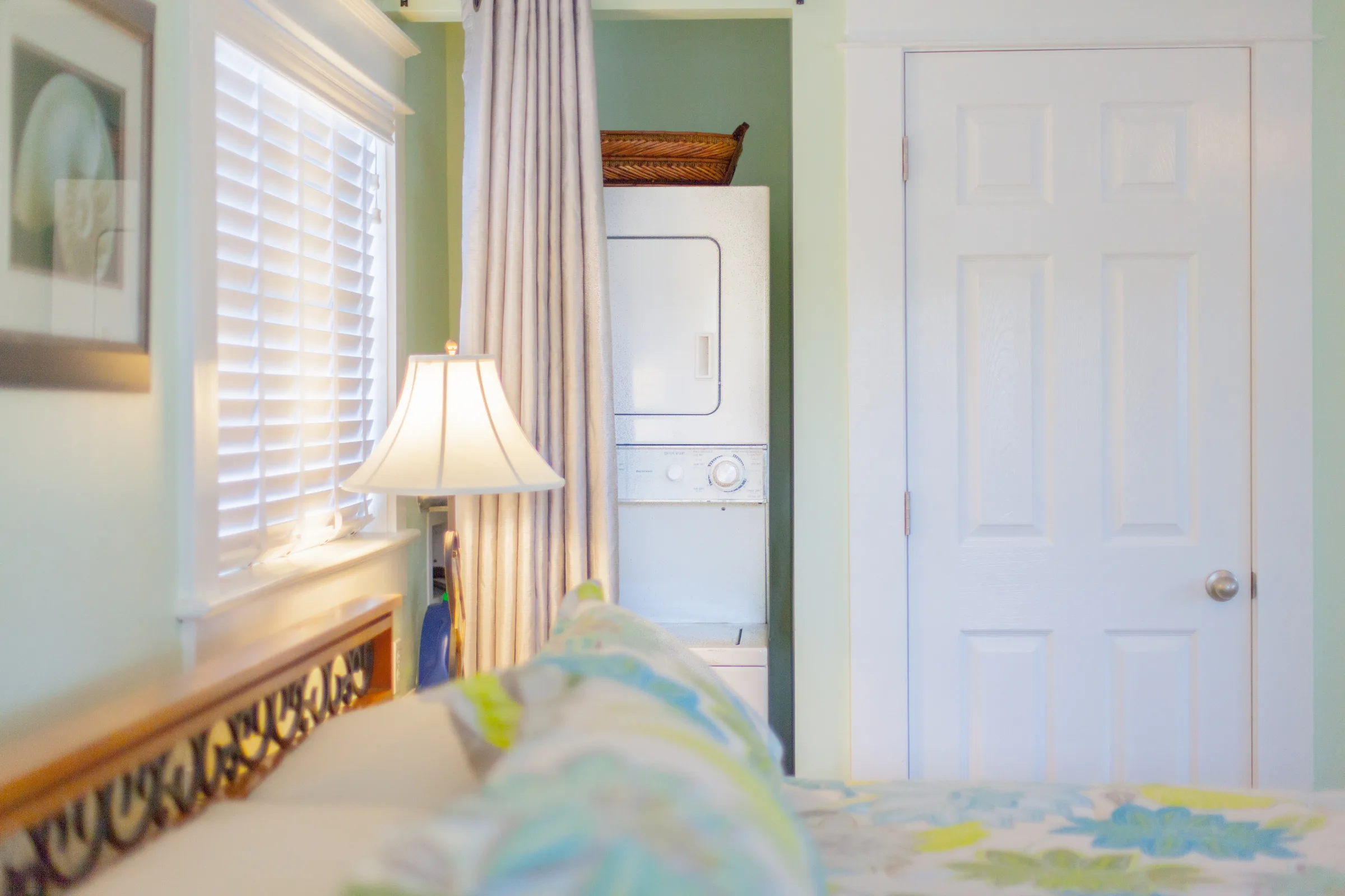 Soft green bedroom corner with lamp, curtains and stacked laundry closet