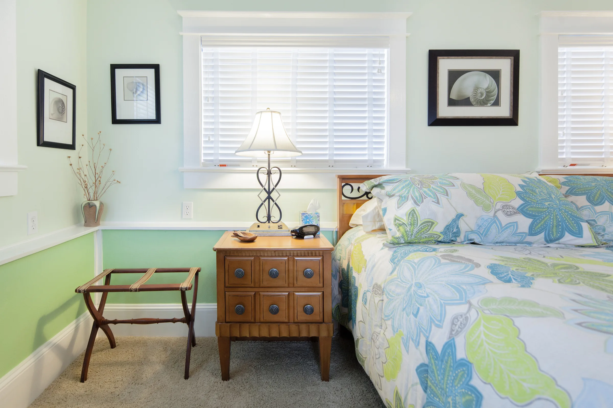 Mint green bedroom with floral quilt, lamp-lit nightstand and luggage rack