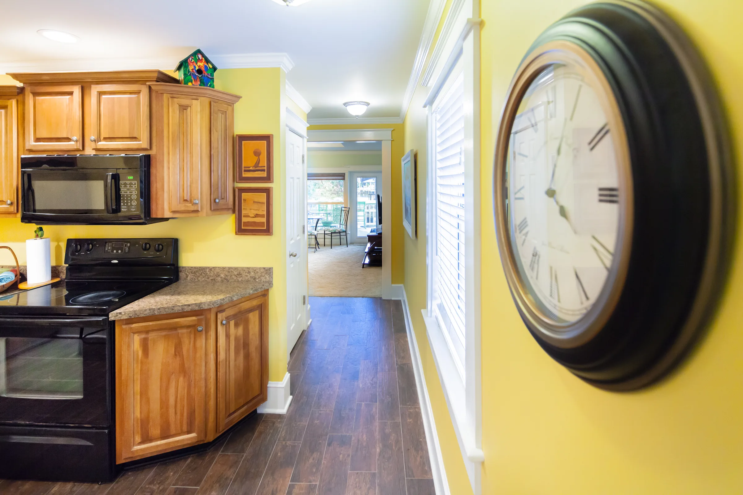 Yellow kitchen hallway with oak cabinets, wall clock and wood-look floors