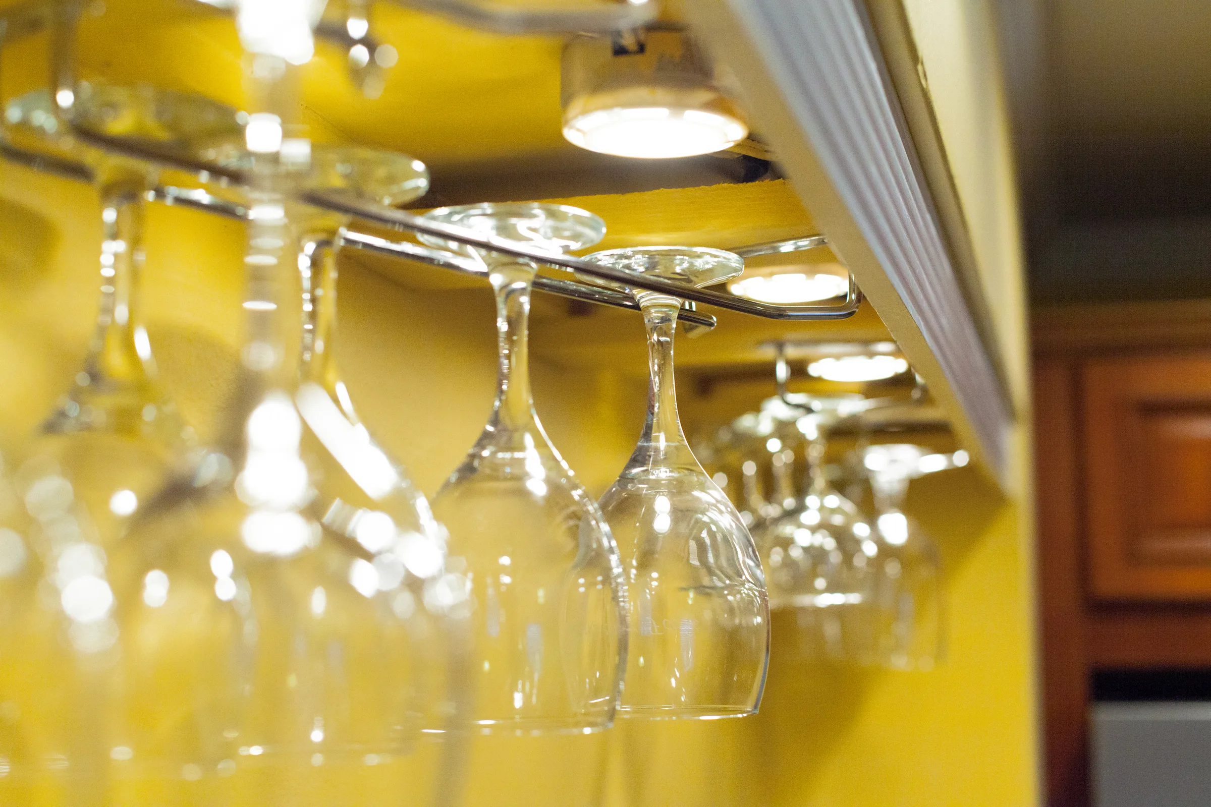Rows of wine glasses hanging in a rack under warm bar lights