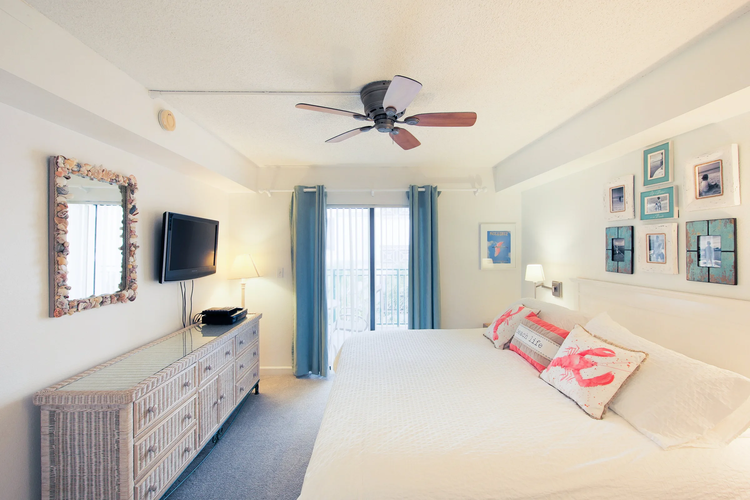 White condo bedroom with king bed, coral accent pillows and balcony door