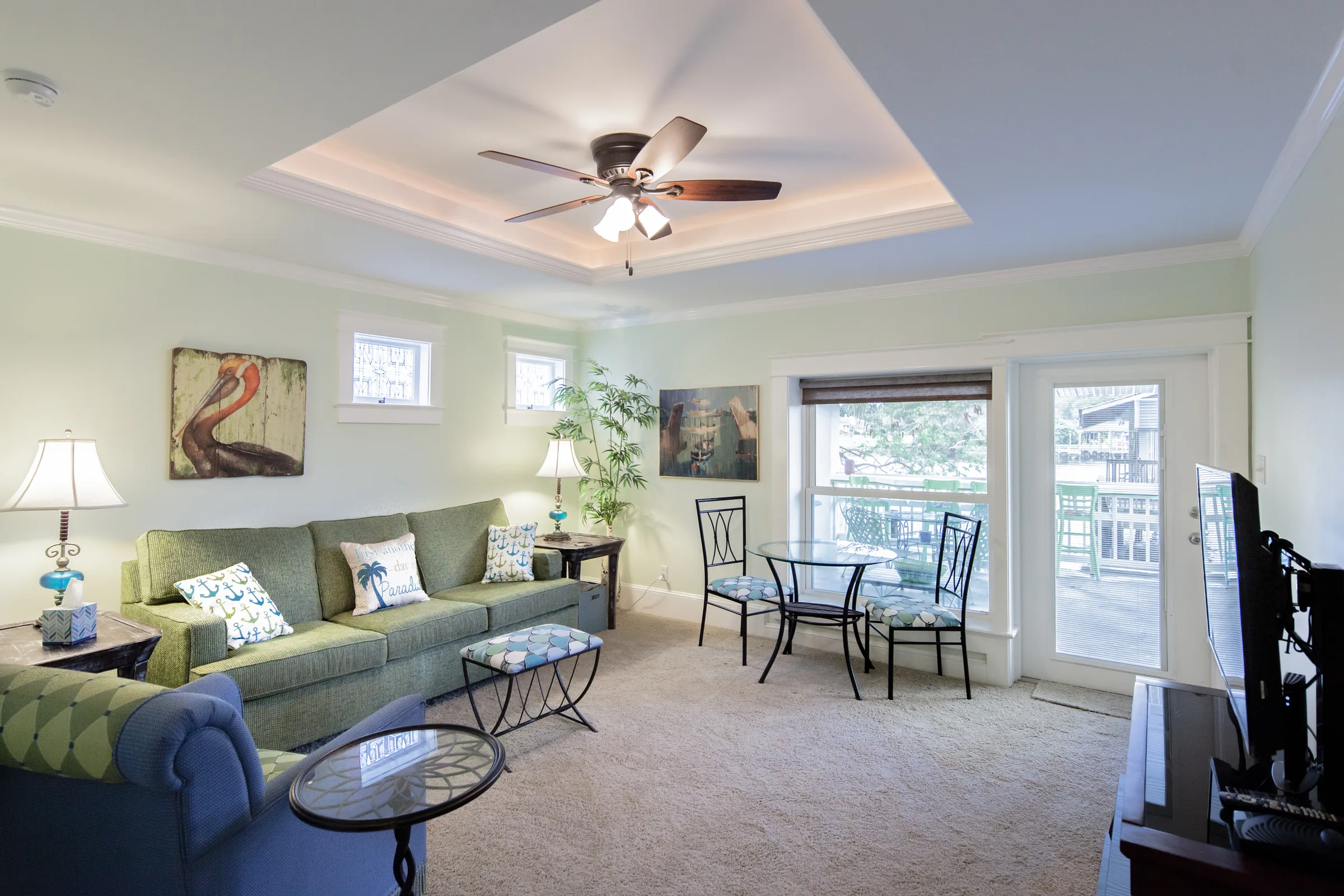Living room with tray ceiling, ceiling fan, and green sectional near porch doors