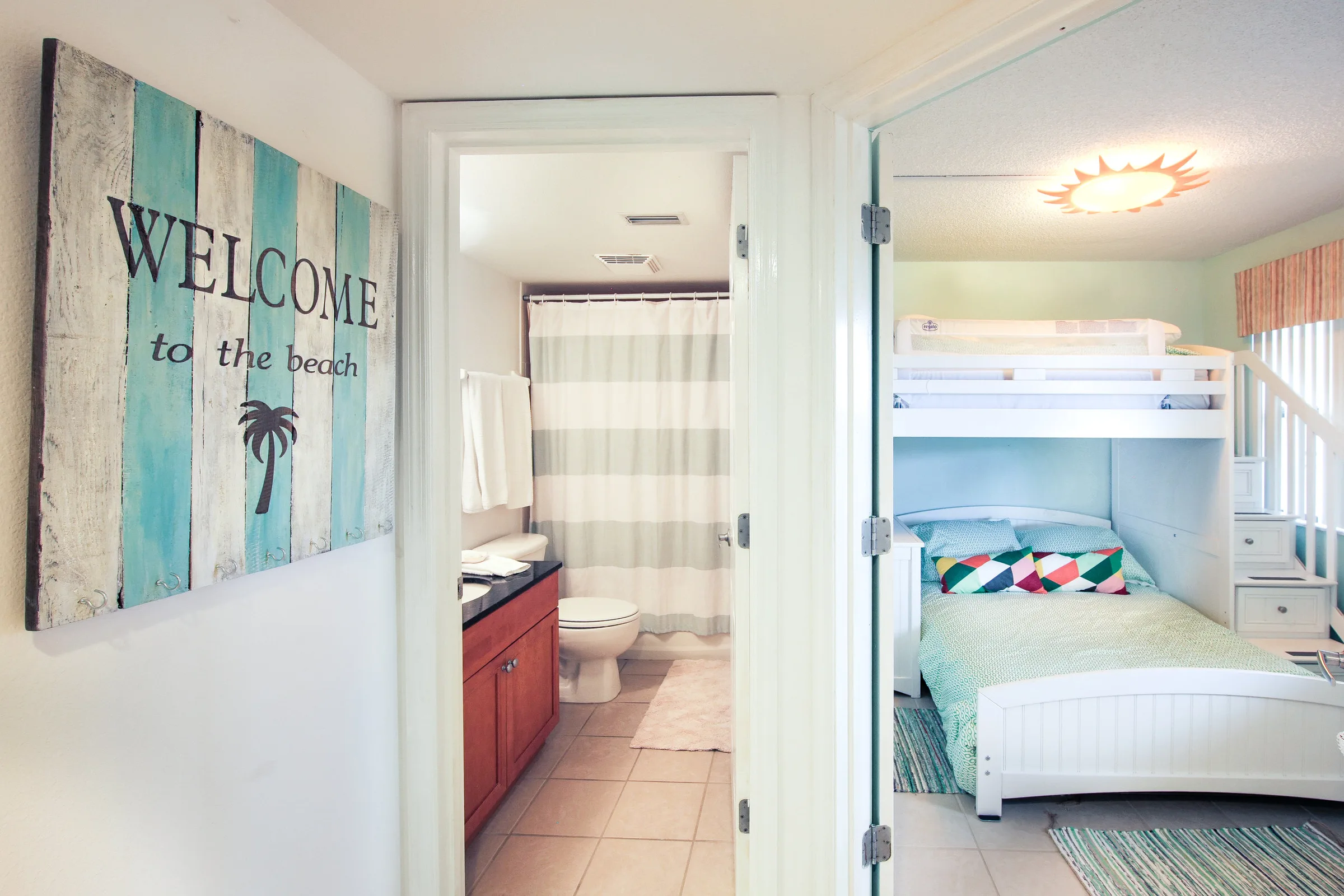 Hallway with beach welcome sign leading to bathroom and bunk-bed bedroom