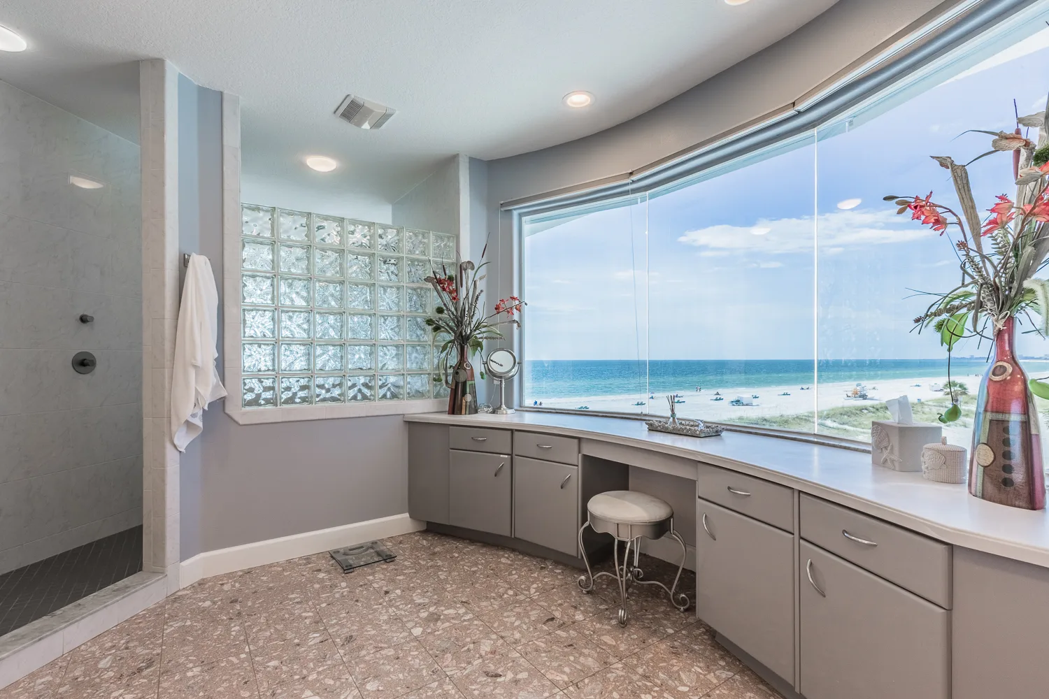 Curved bathroom vanity beneath panoramic window with sweeping beach view