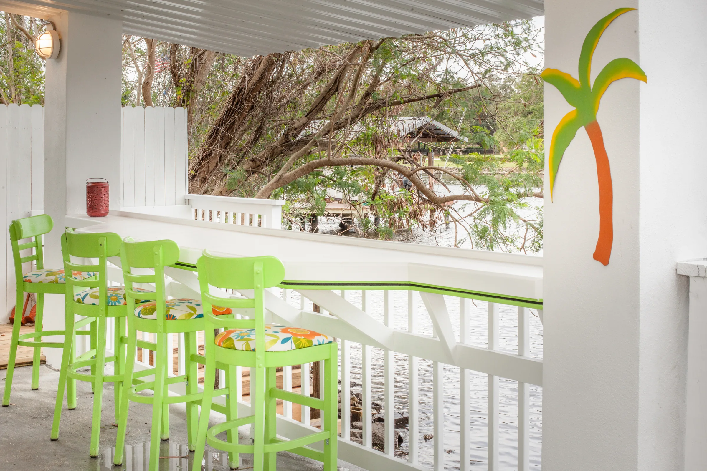Lime green bar stools line a white porch railing overlooking the water