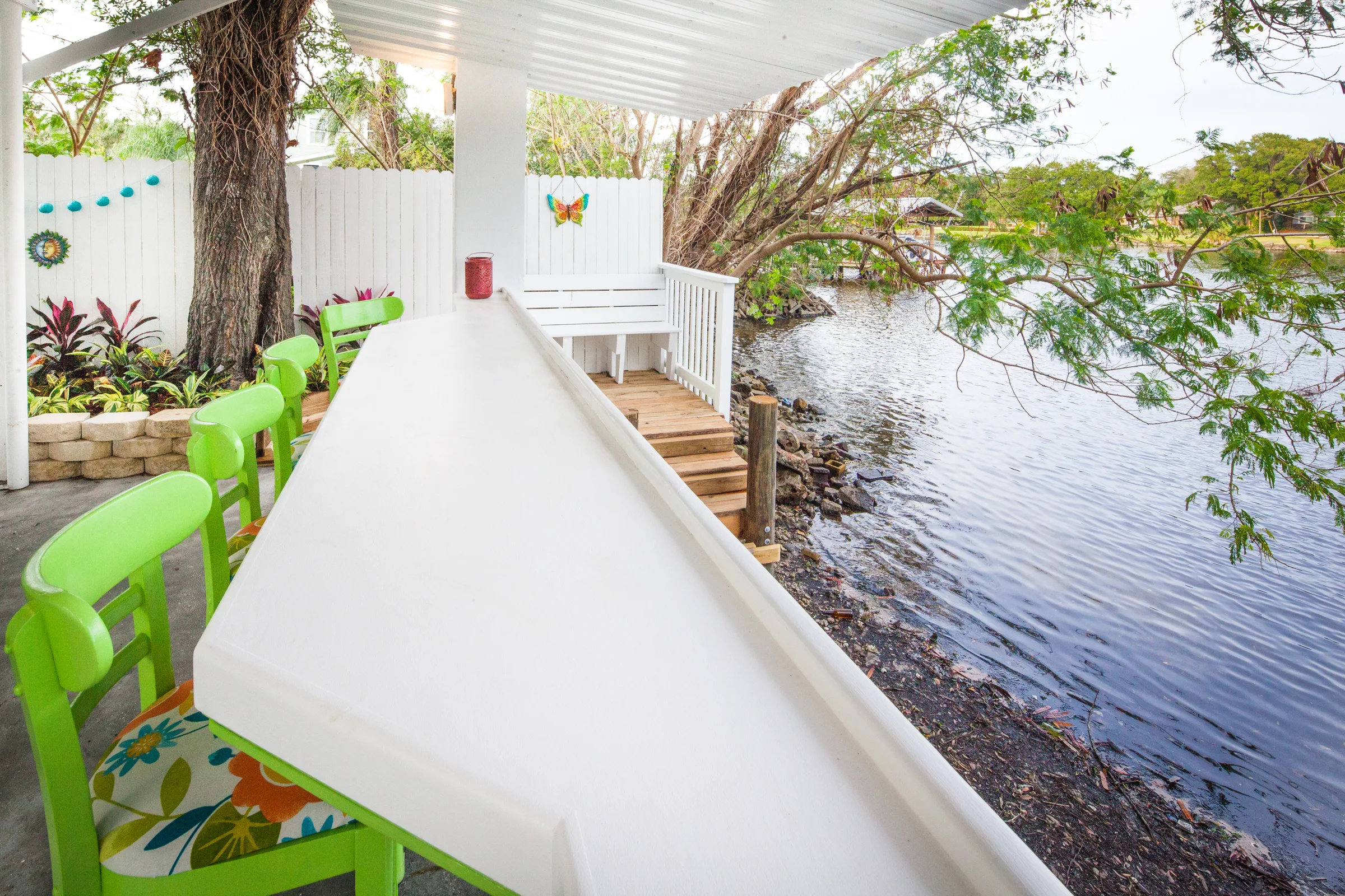Covered waterfront porch with green chairs beside a wooden dock