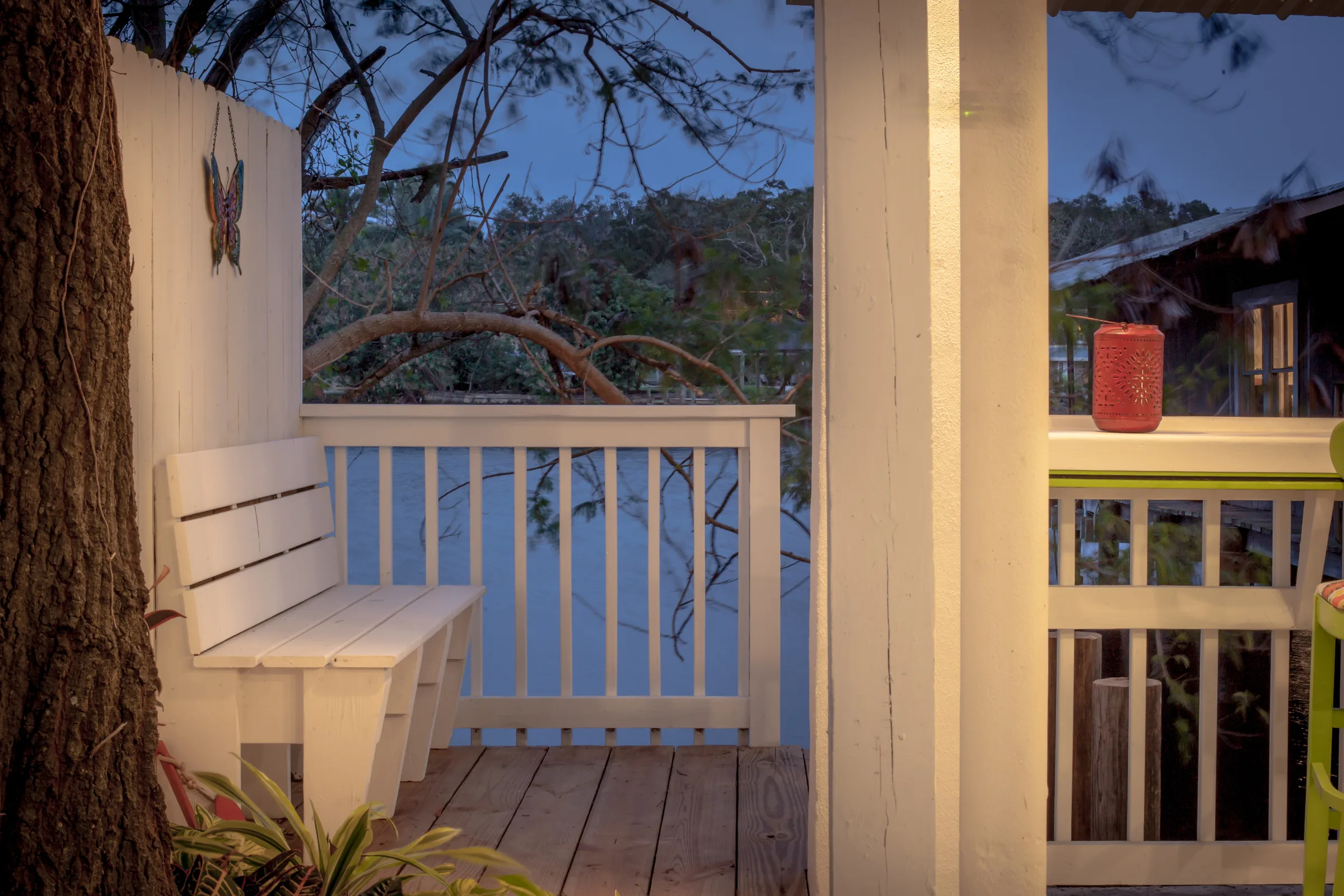 White porch bench at dusk overlooking calm water through the railing