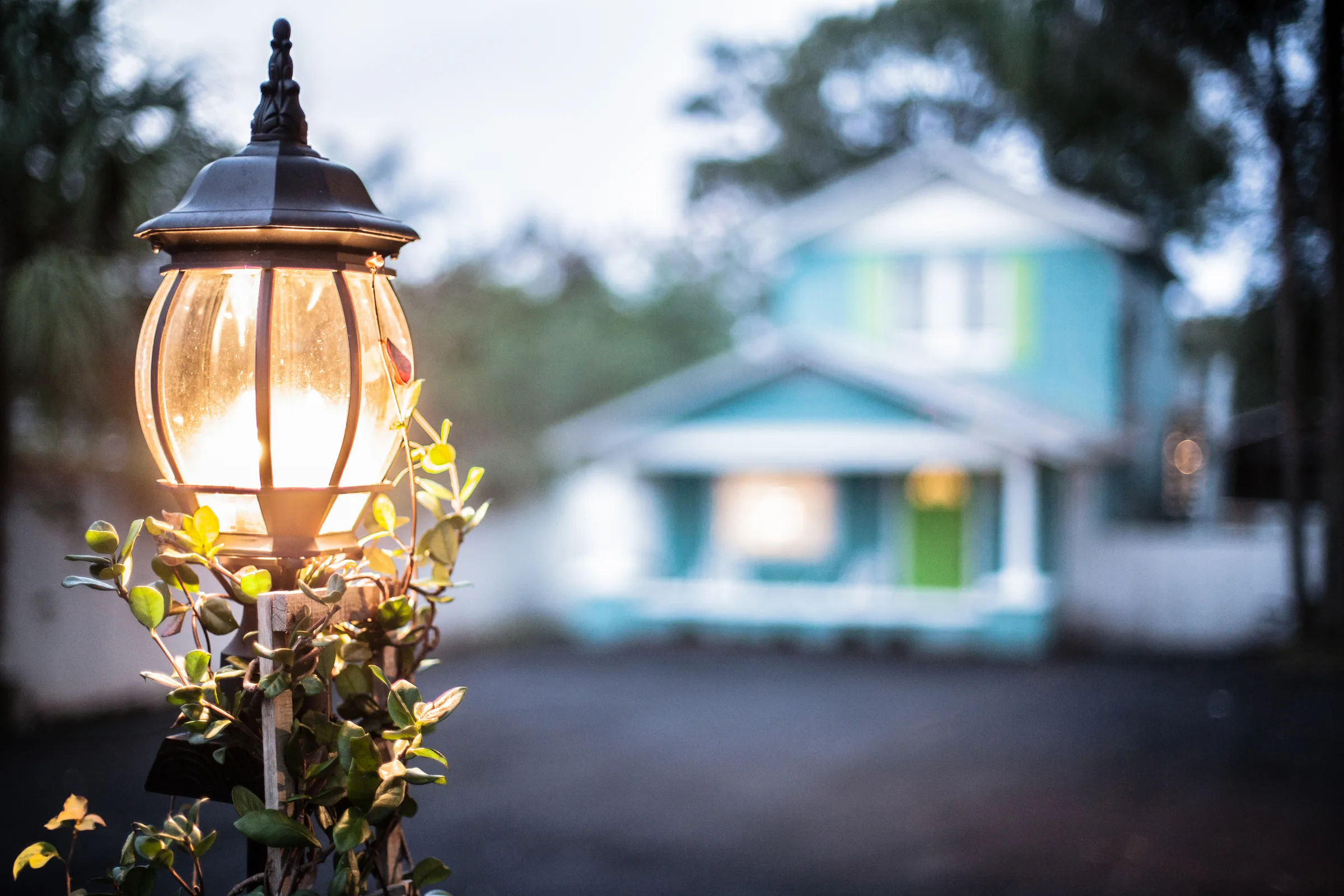 Glowing lamppost at dusk with a turquoise beach house in the background