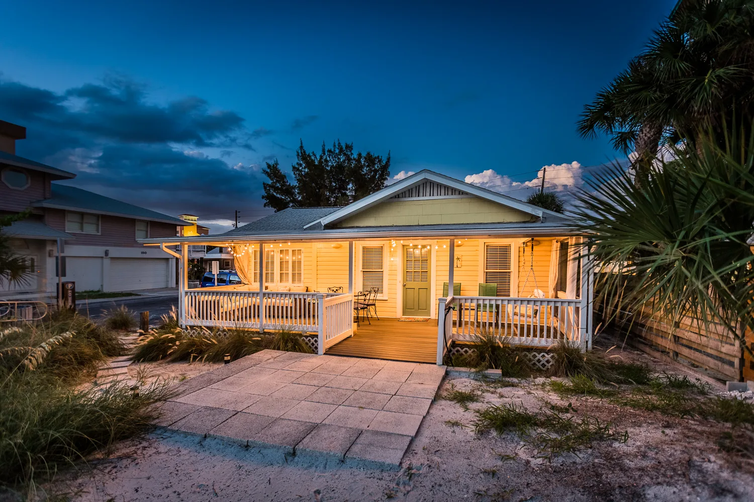 Beach cottage exterior at twilight with warmly lit wraparound porch