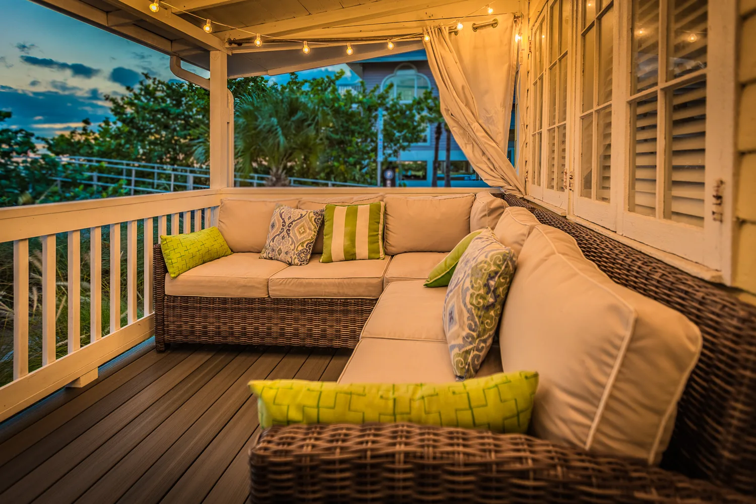 Wicker sectional with green pillows on a porch under string lights