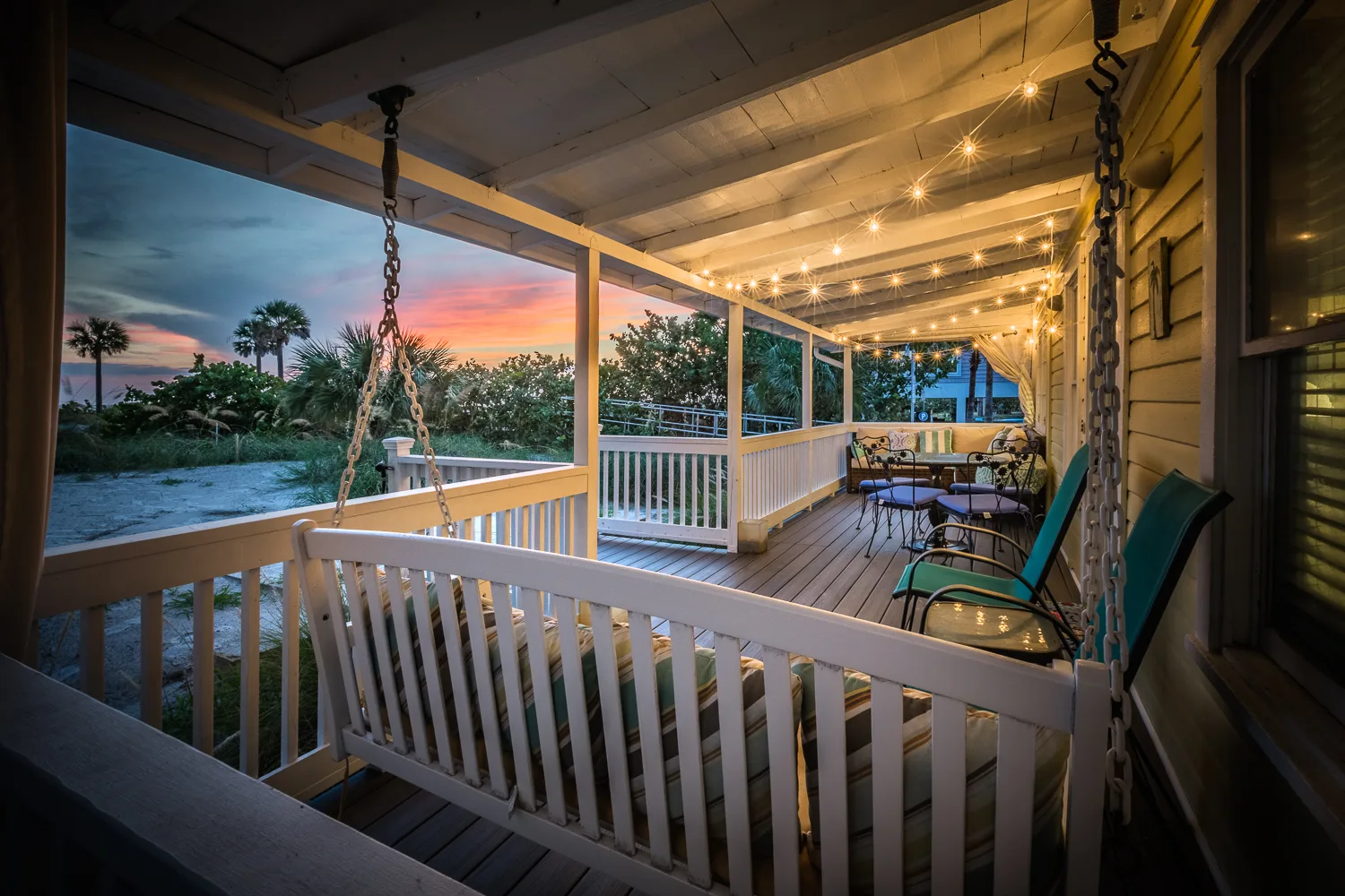 Porch swing and string lights facing dunes at colorful sunset