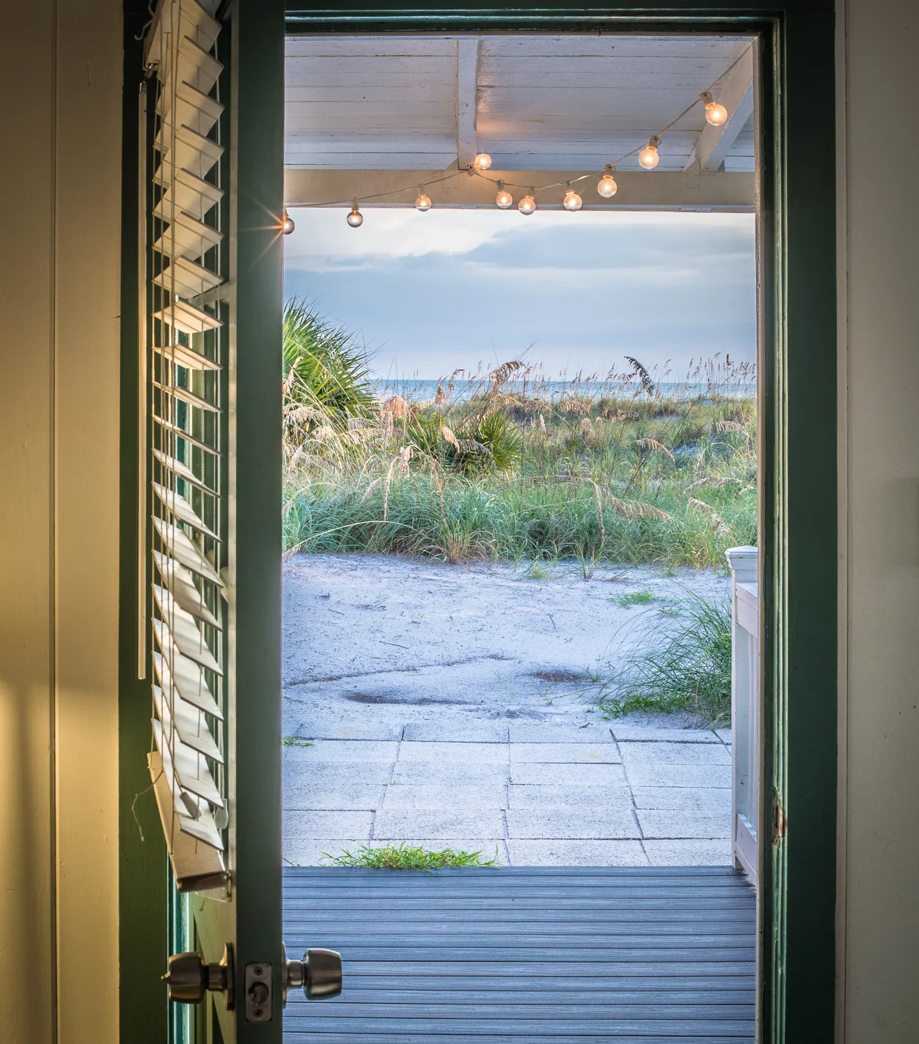 Open cottage door framing a sandy path through dunes to the sea